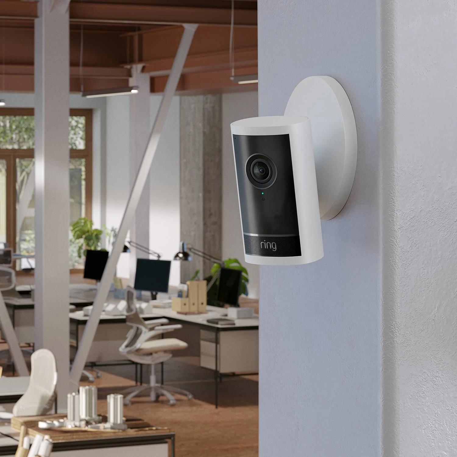 Ring video doorbell mounted on a wall in an office space with desks and computers.