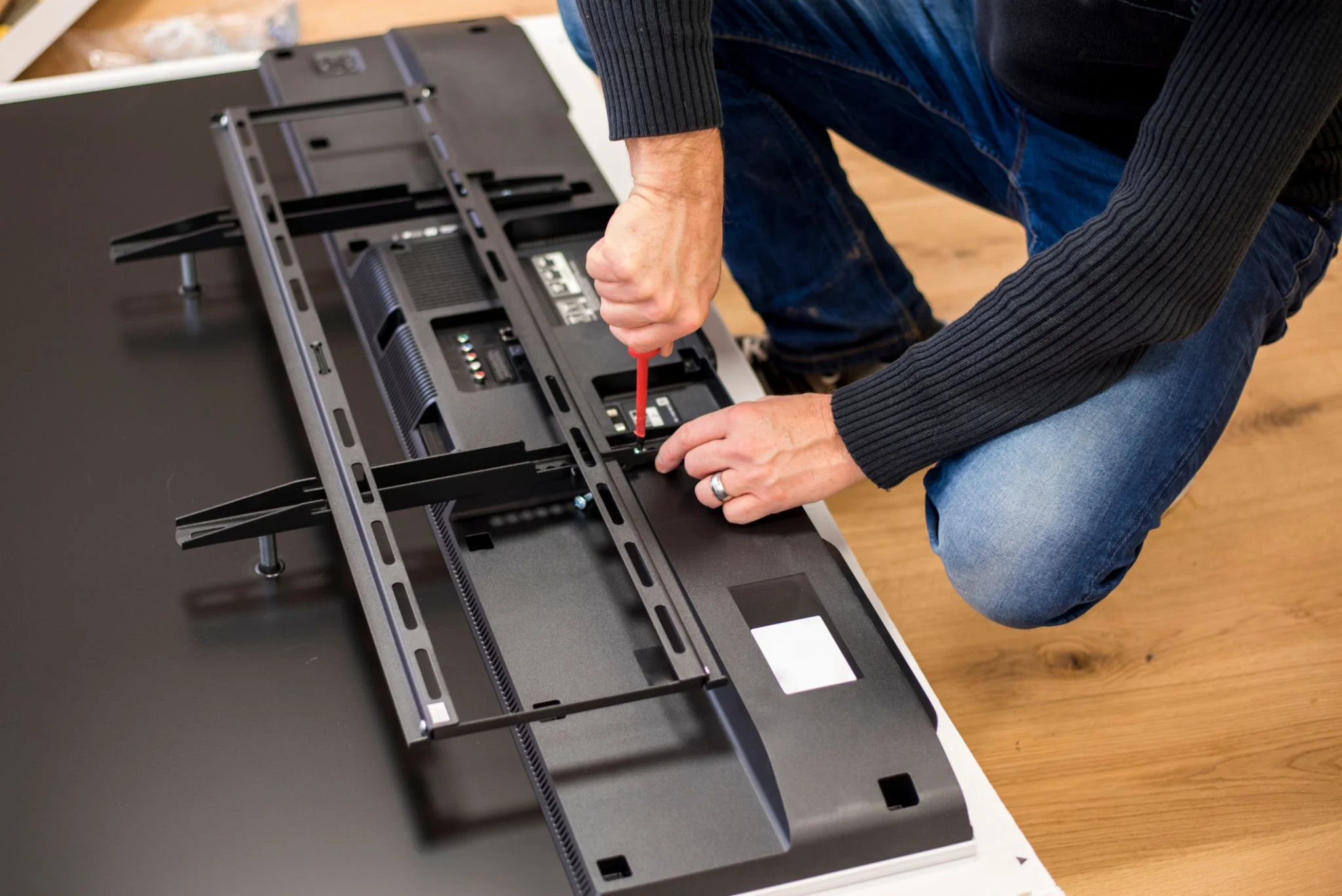 Person installing or repairing a flat-screen TV or monitor on a black surface using a screwdriver.