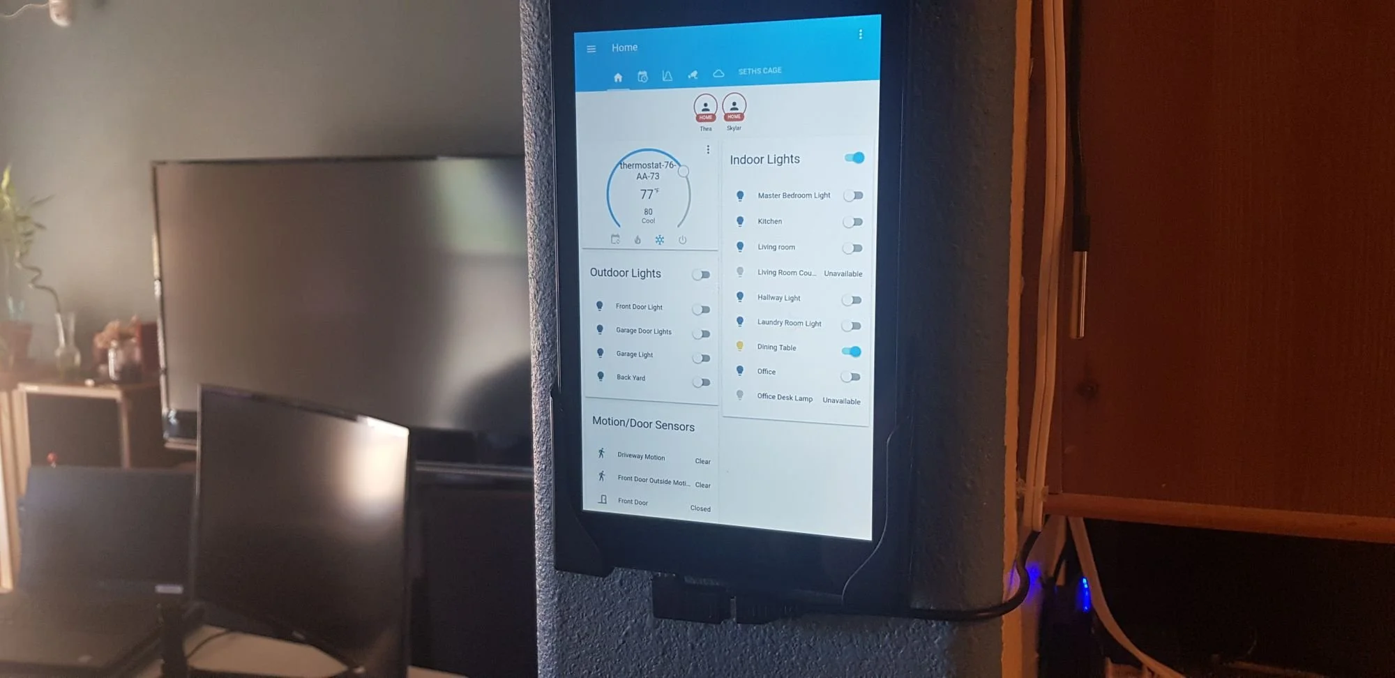 Smart home control tablet mounted on wall displaying indoor and outdoor lights, thermostat, and motion sensors.