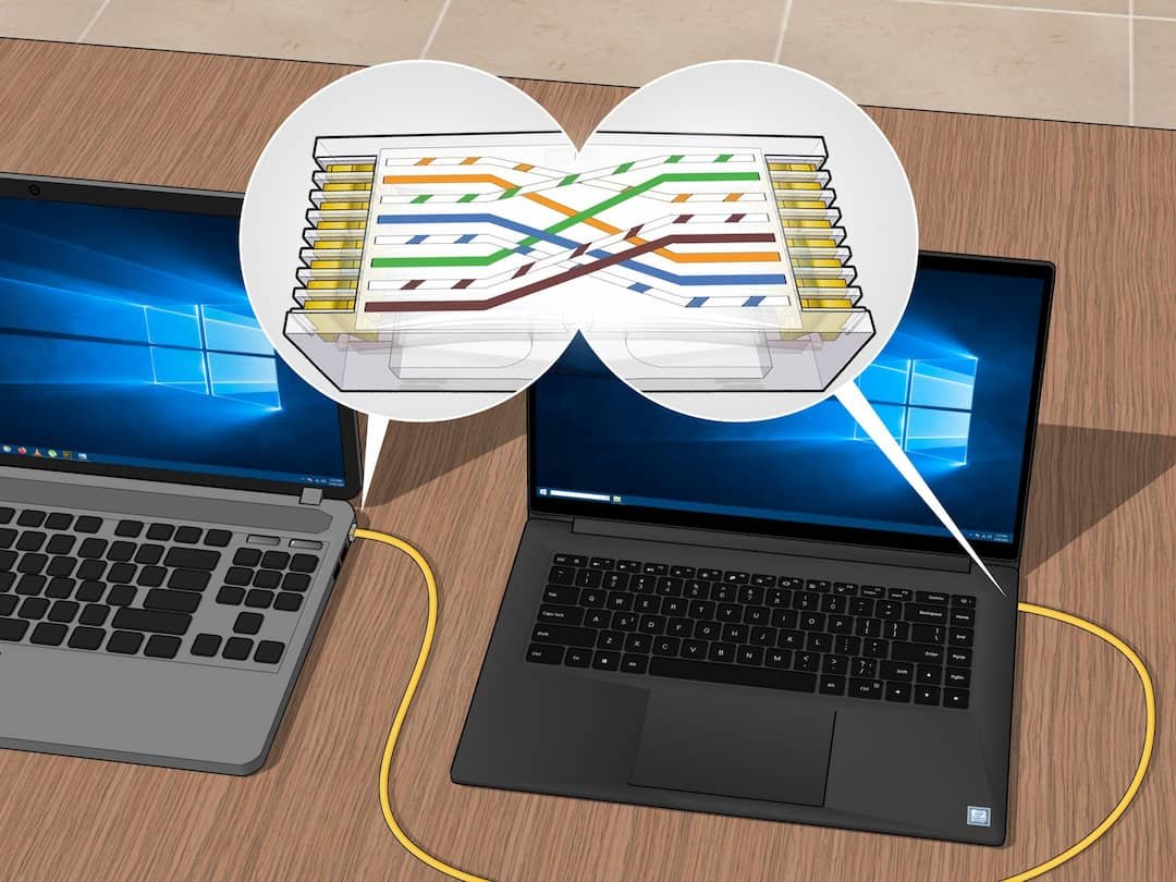 Two laptops connected by yellow cables on a wooden table. The laptop on the left has a Windows screen. A speech bubble with a diagram depicting a complex train track system with multiple colored lines is shown above the laptops.
