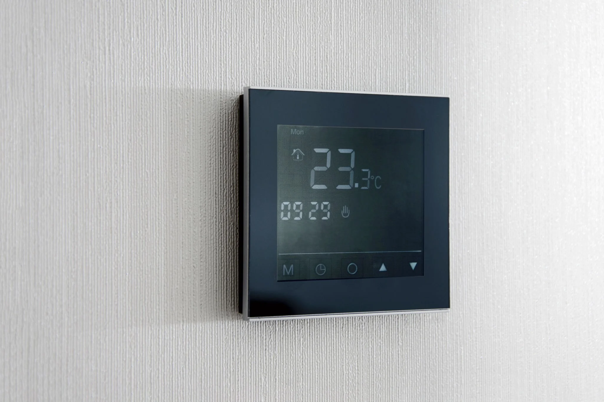 Digital thermostat mounted on a white textured wall displaying a temperature of 23.3°C.