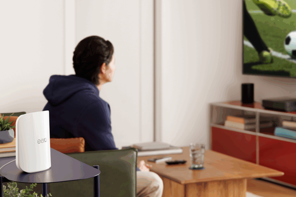 A woman sitting on a couch watching TV, with an air purifier on a nearby table, a glass of water, and a TV remote on a wooden table, in a modern living room.