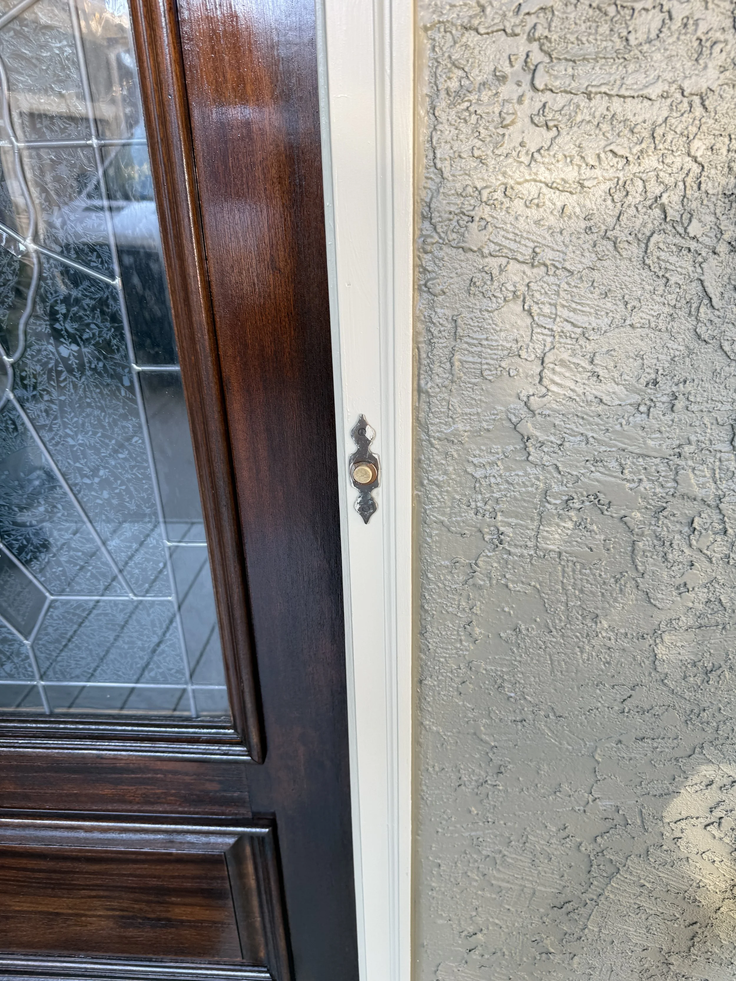 Close-up of a front door frame with a missing door handle or lock, showing the door and a textured exterior wall.