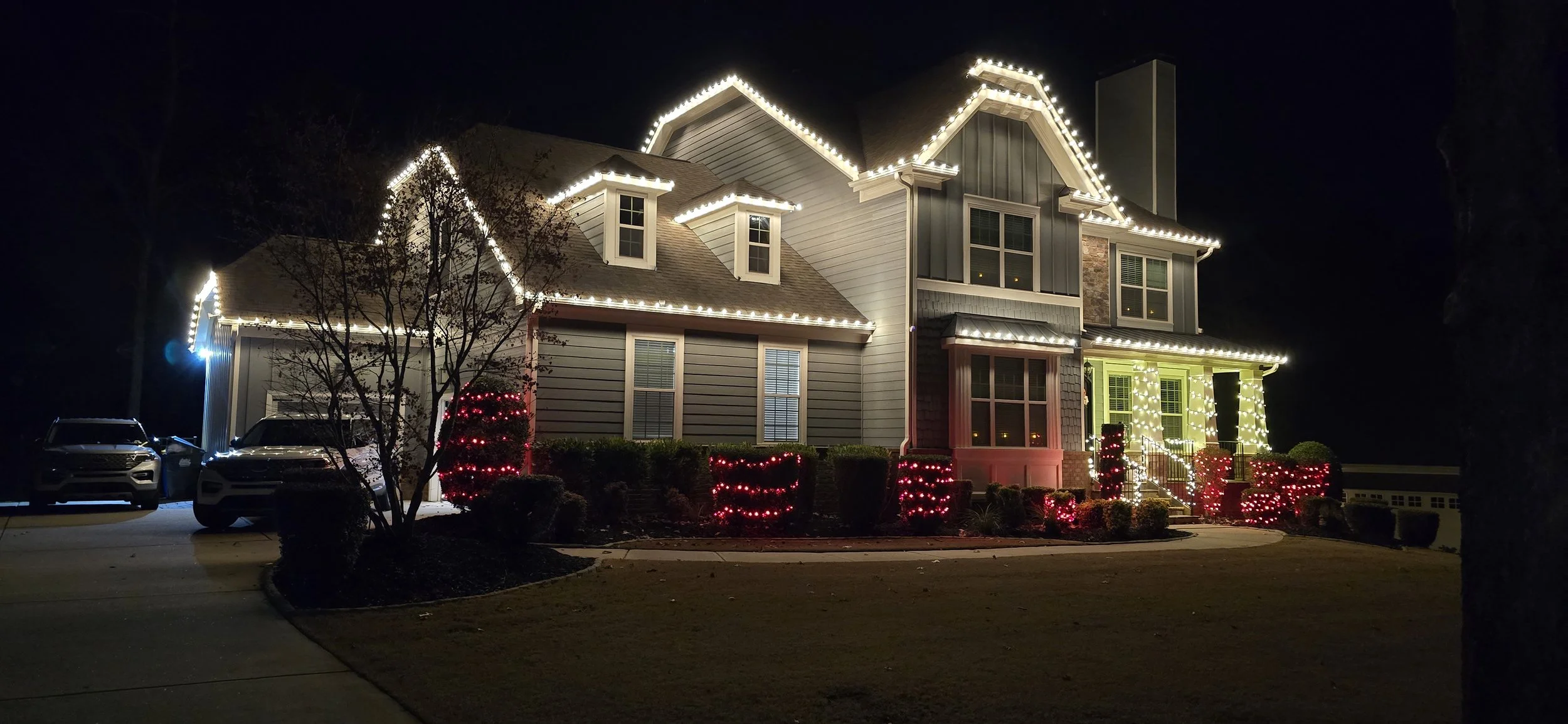 Two-story Acworth GA home with warm white Christmas lights installed along the roofline, windows and landscaping