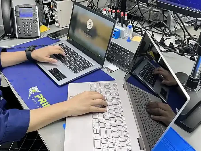 A person working at a tech workspace with multiple laptops, monitors, and electronic accessories on a cluttered desk.