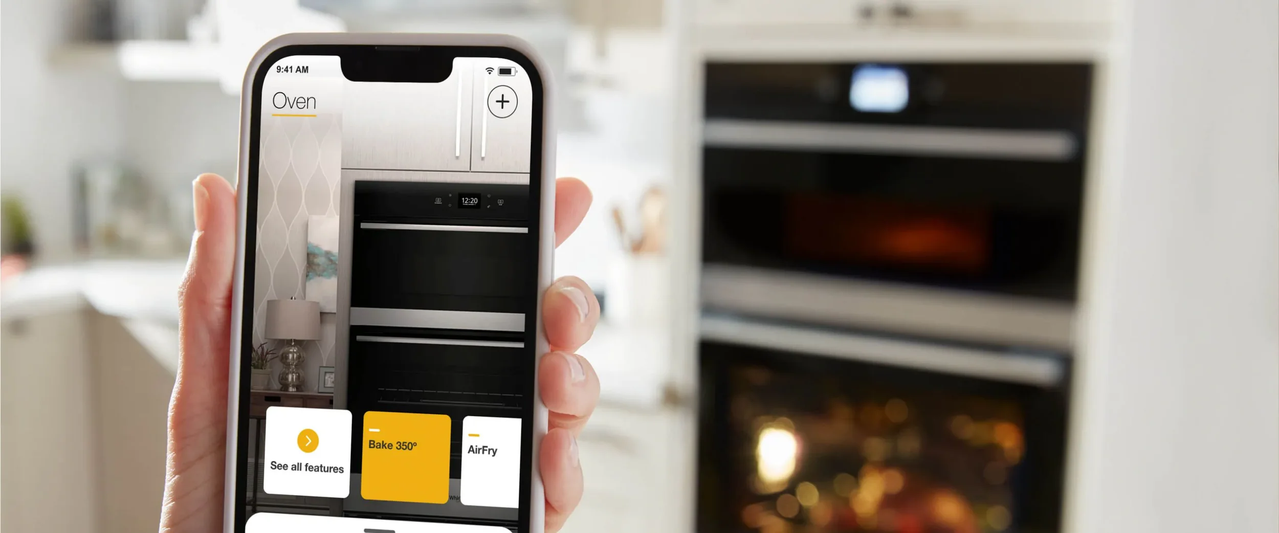 Person holding a smartphone in front of a kitchen oven, using an app to operate the oven.