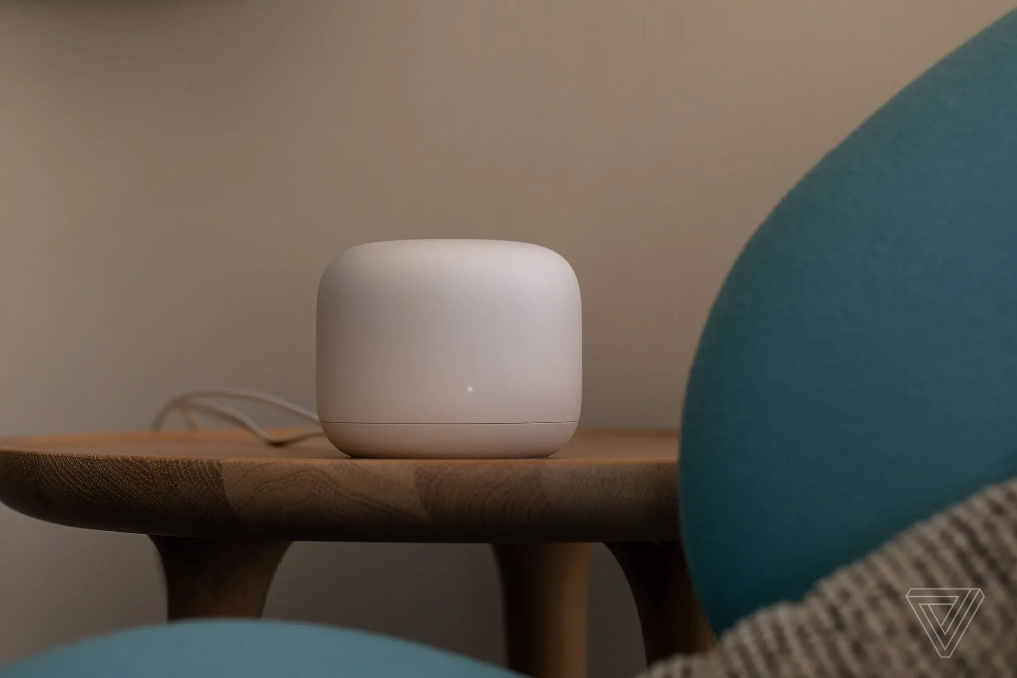 A white smart speaker on a wooden table, with a blue pillow and part of a person's legs in the foreground.