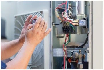 Technician repairing or inspecting the interior of an electrical or HVAC control panel with various wires and components.