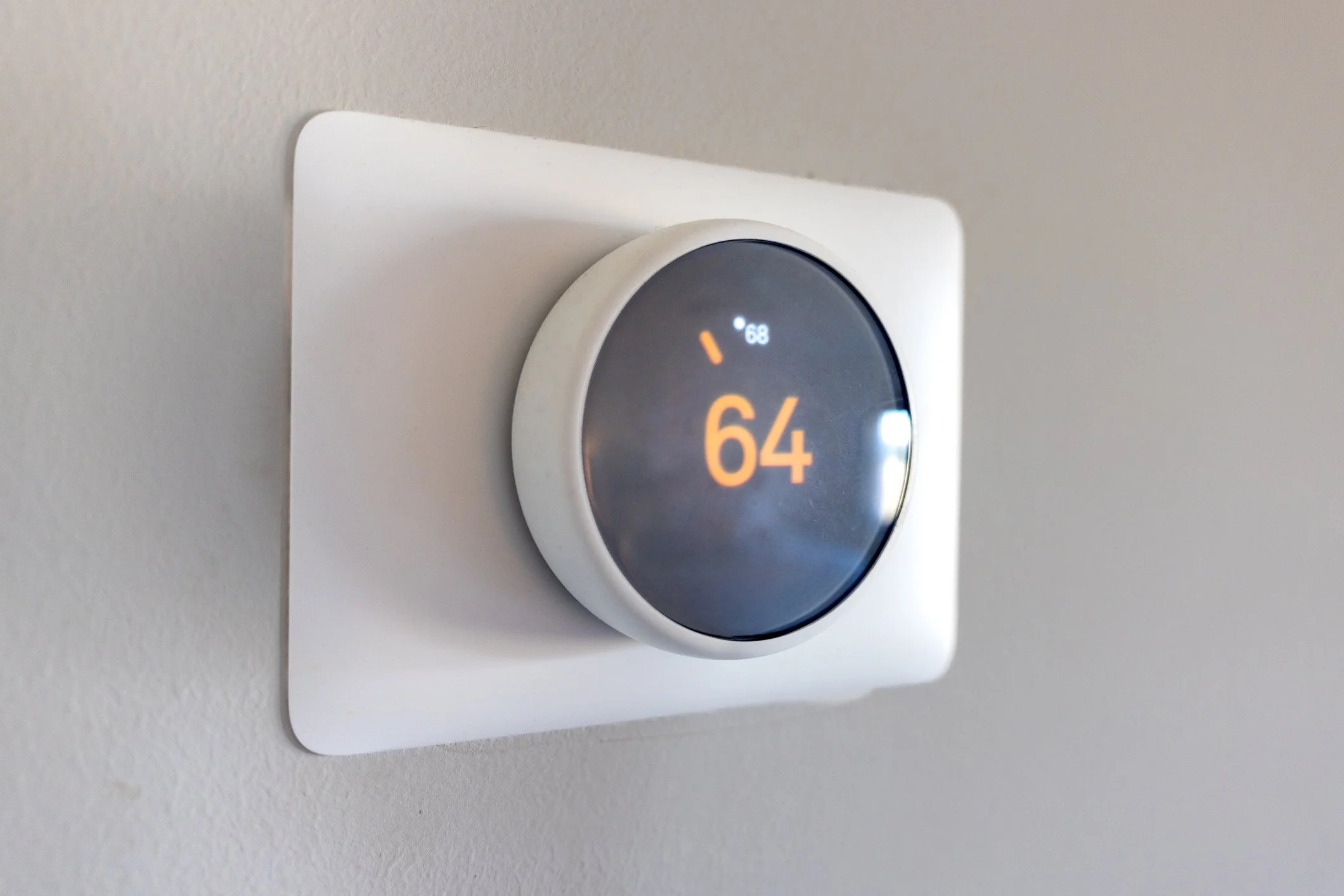 Thermostat on a white wall displaying a temperature of 64 degrees Fahrenheit.