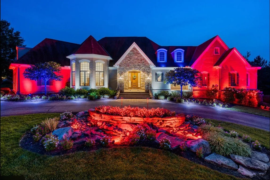 Large house illuminated with colorful exterior lights at night, decorated for a celebration or holiday.