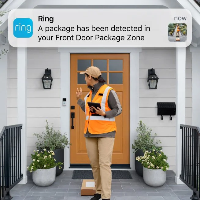 A delivery person in an orange vest and beige cap standing in front of a house, using a device to scan or confirm a package delivery. The house has a wooden door, two black lantern-style lights, and potted plants on either side of the entrance.