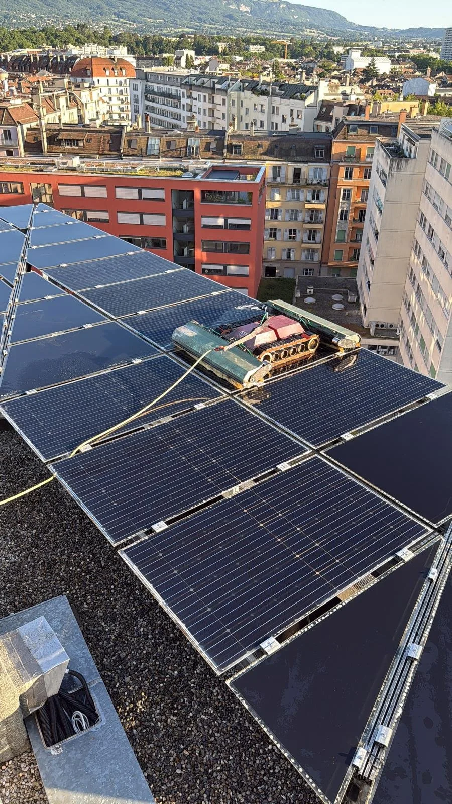 Panneaux solaires installés sur le toit d'un immeuble en milieu urbain, avec un robot nettoyeur à énergie solaire en fonctionnement.