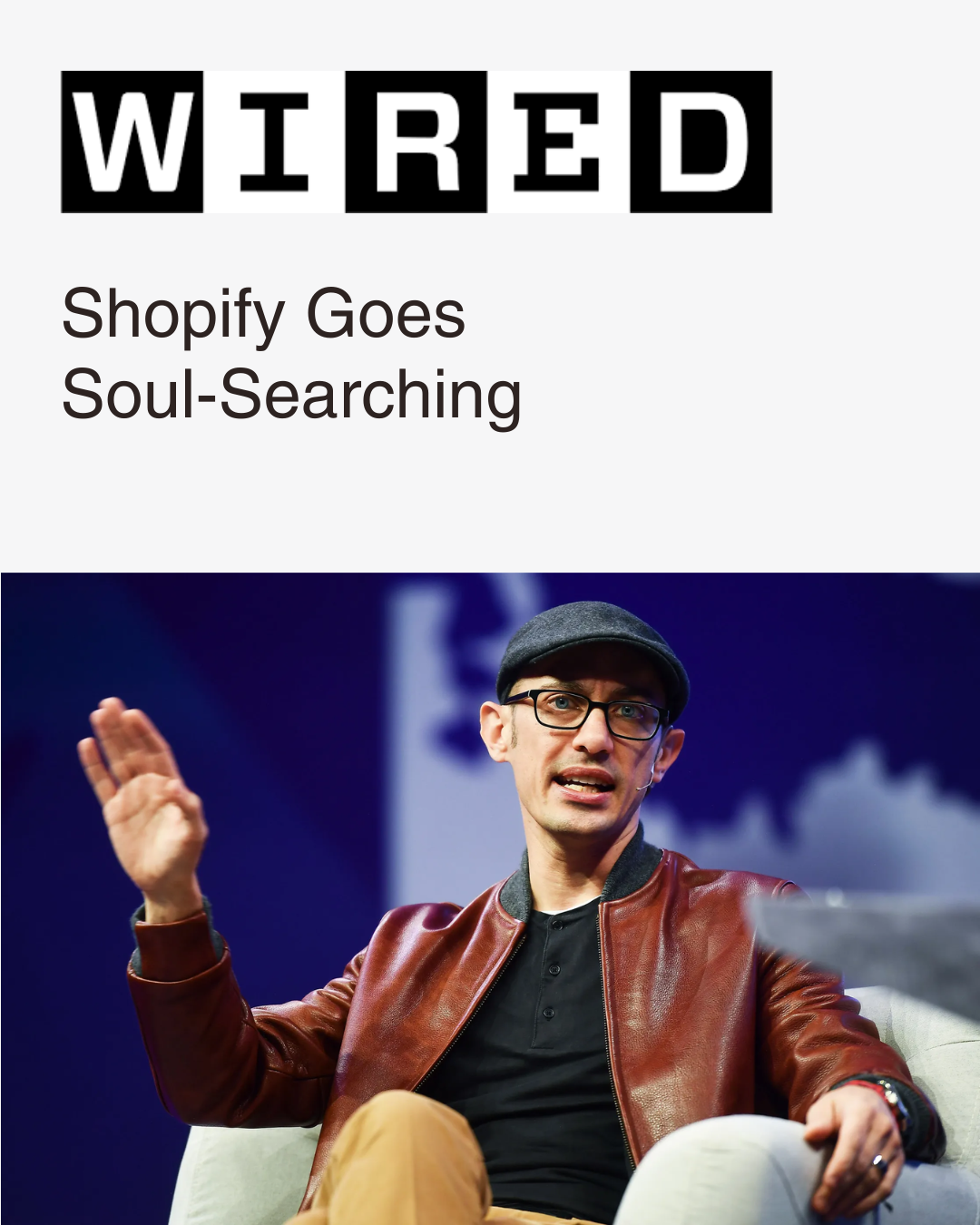 WIRED article titled "Shopify goes soul-searching". CEO Tobi Lutke in glasses, a gray flat cap, a brown leather jacket, and a black shirt, sitting on a light-colored chair, speaking and gesturing with his right hand.