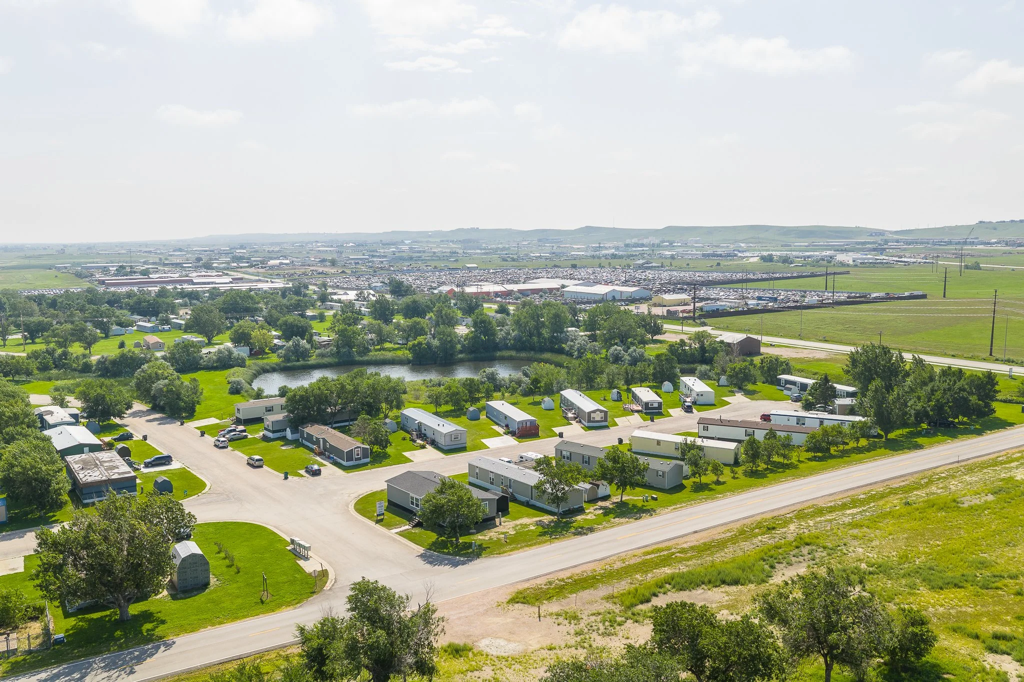 Aerial view of a neighborhood with houses, trees, a pond, and a distant industrial area.