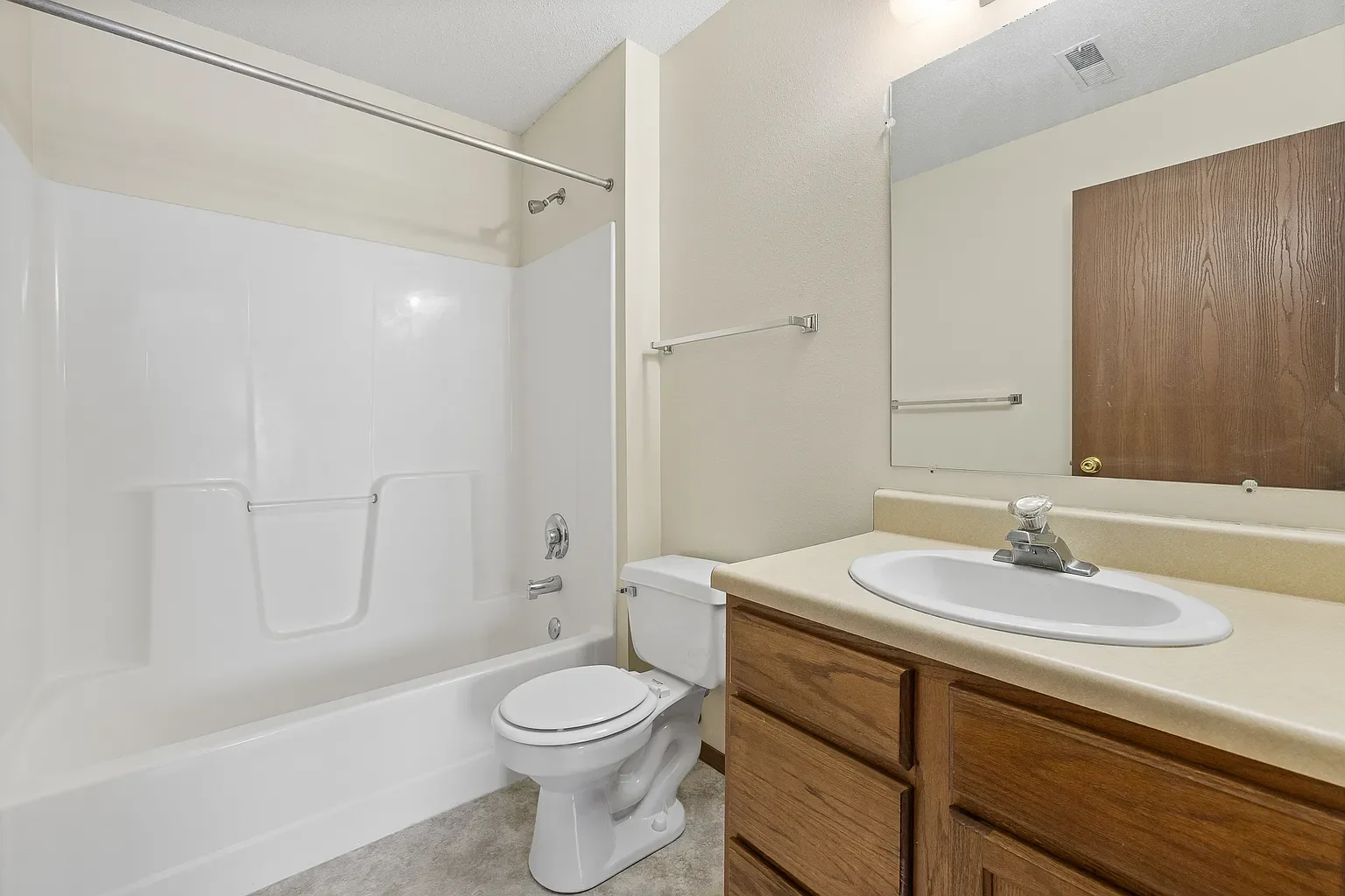 Bathroom with bathtub and shower, toilet, mirror, and wooden vanity with sink.