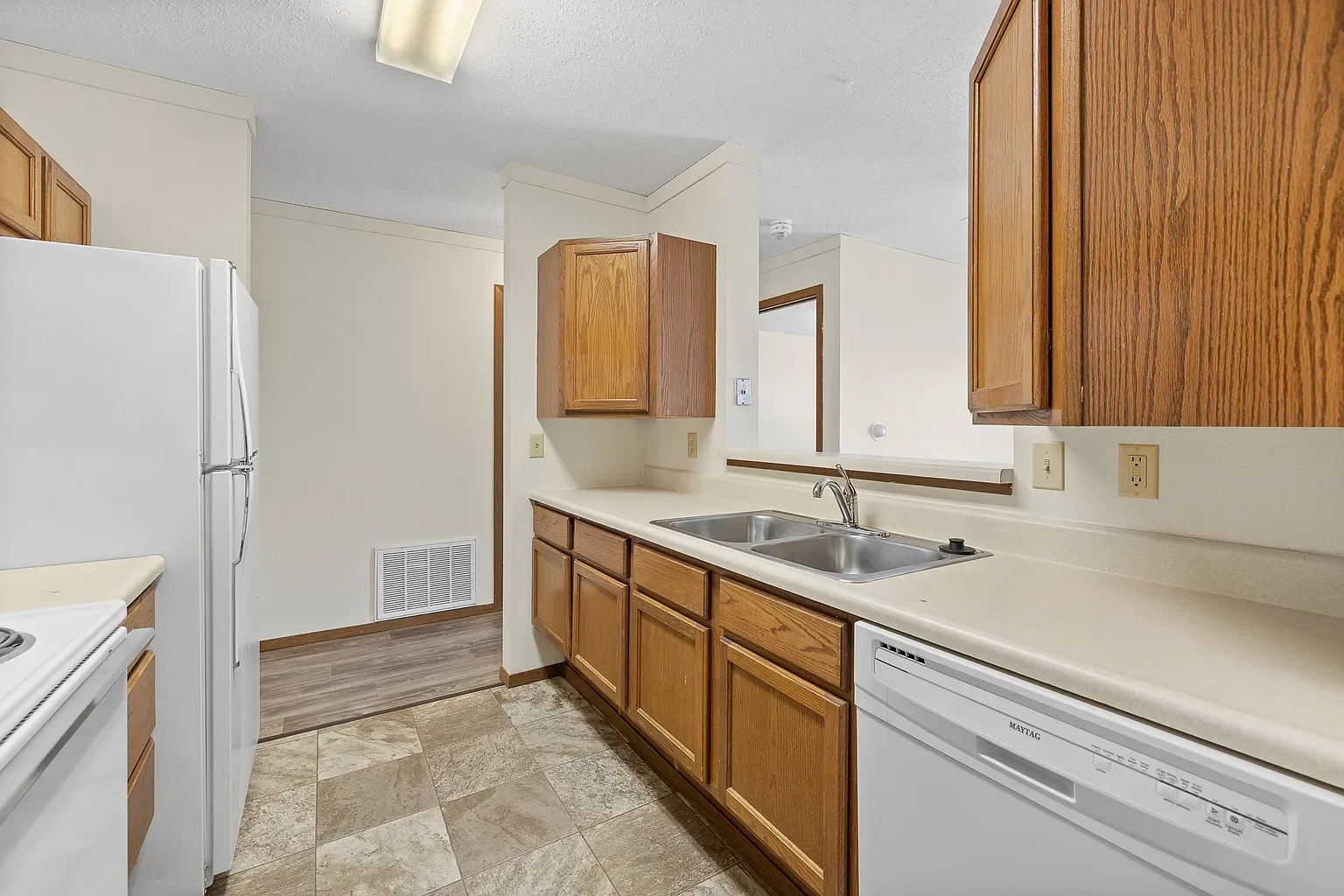 Kitchen with wooden cabinets, white refrigerator, double sink, dishwasher, and beige countertops.