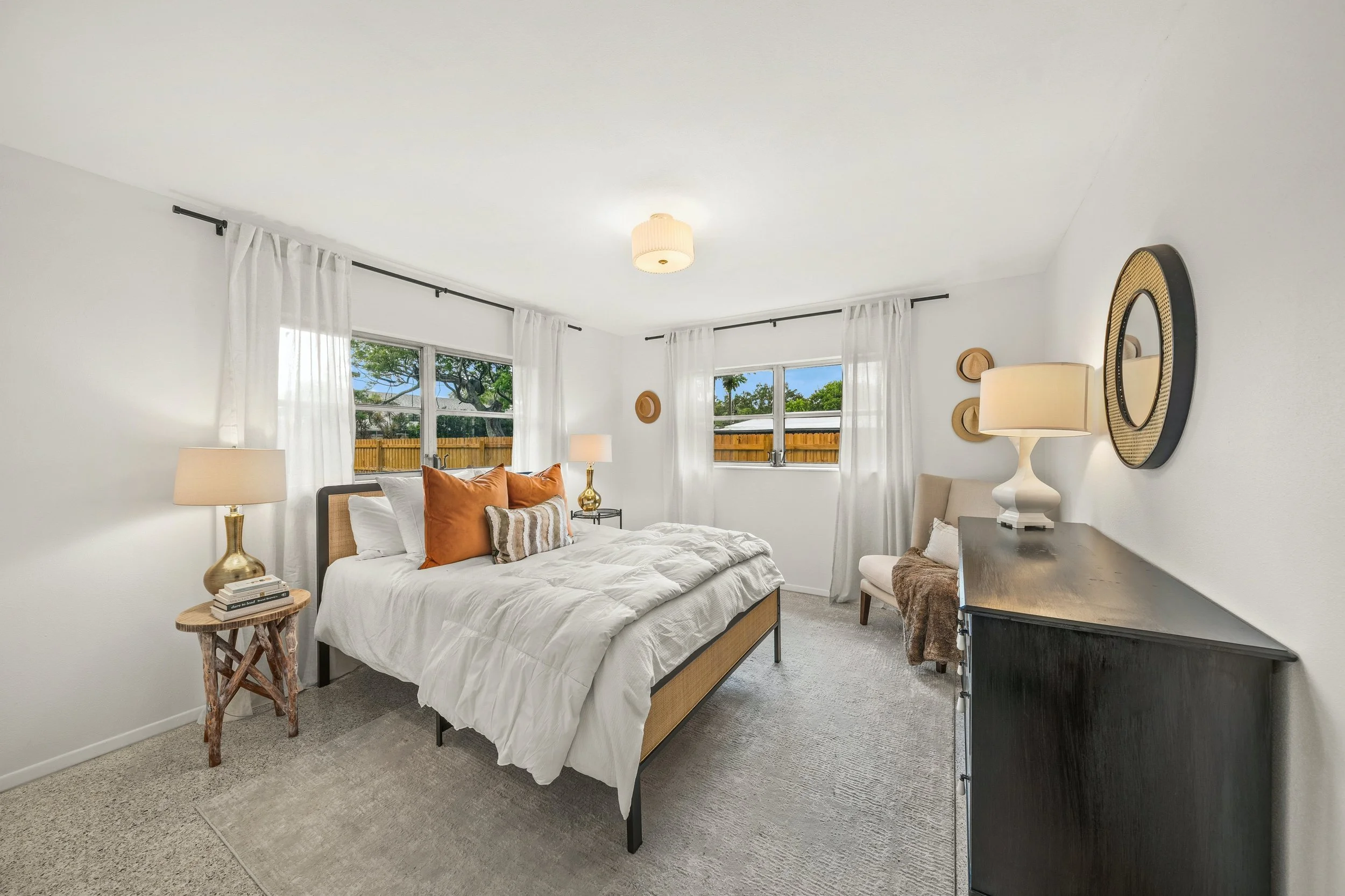 Bright bedroom with a bed, nightstand, lamps, and windows with white curtains