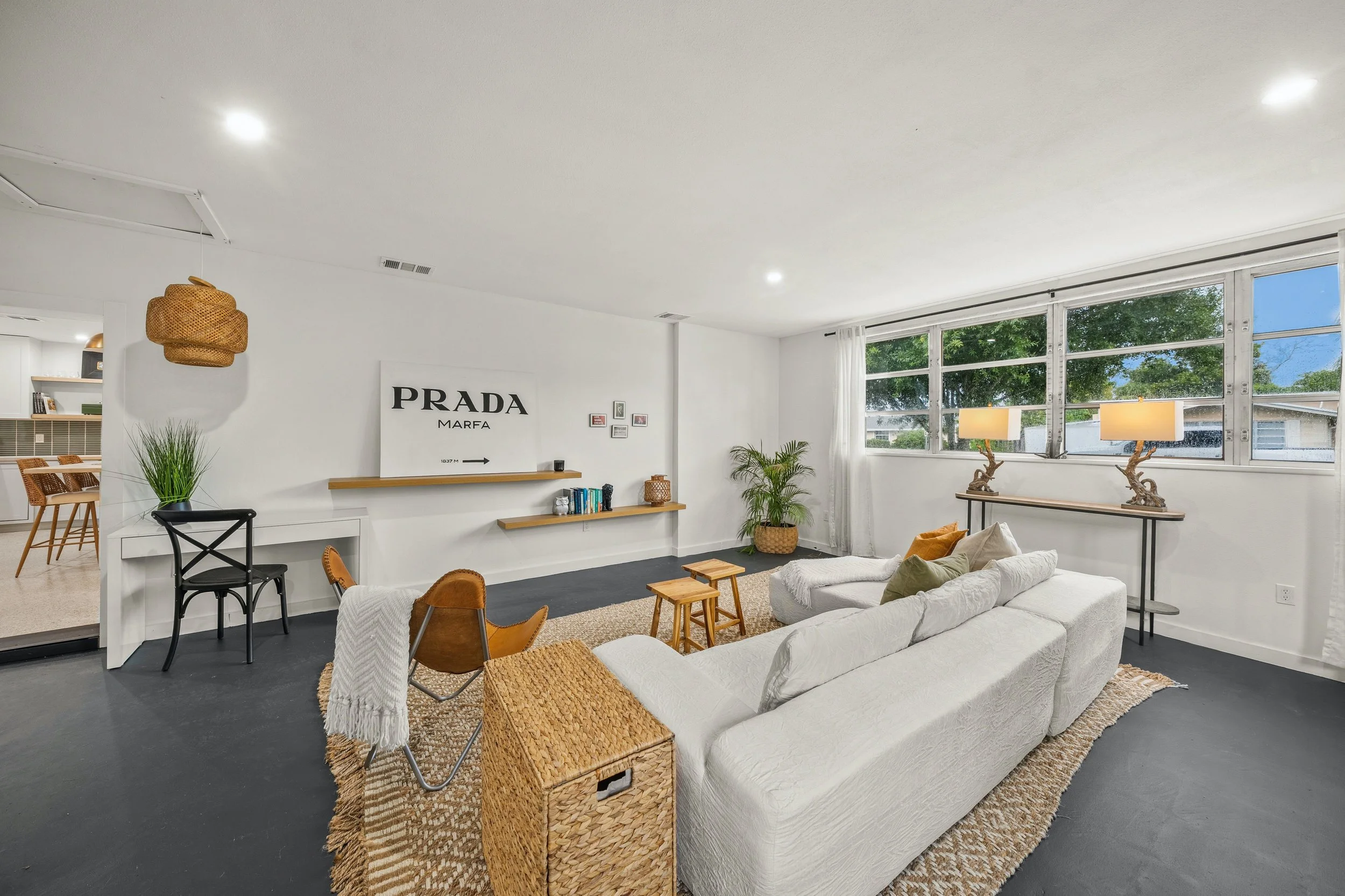 Bright living room with large window, white walls, white sofa, wicker storage box, plants, and modern decor.