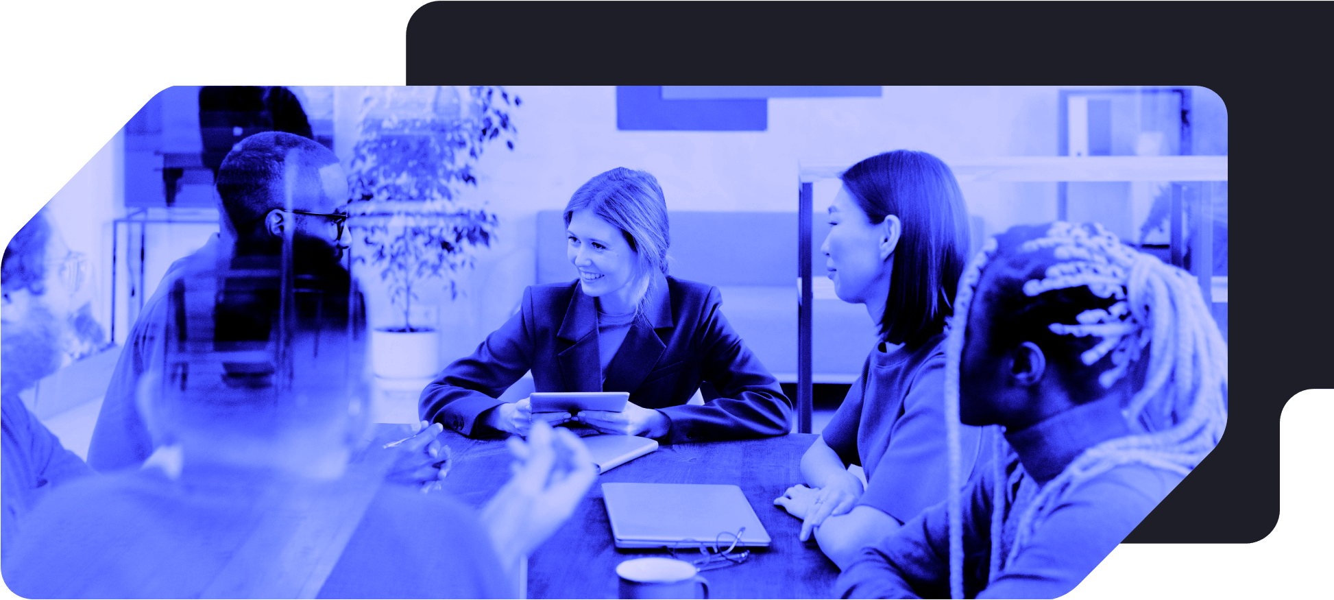 Group of five diverse people having a meeting at a table in an office, with one woman speaking while others listen.