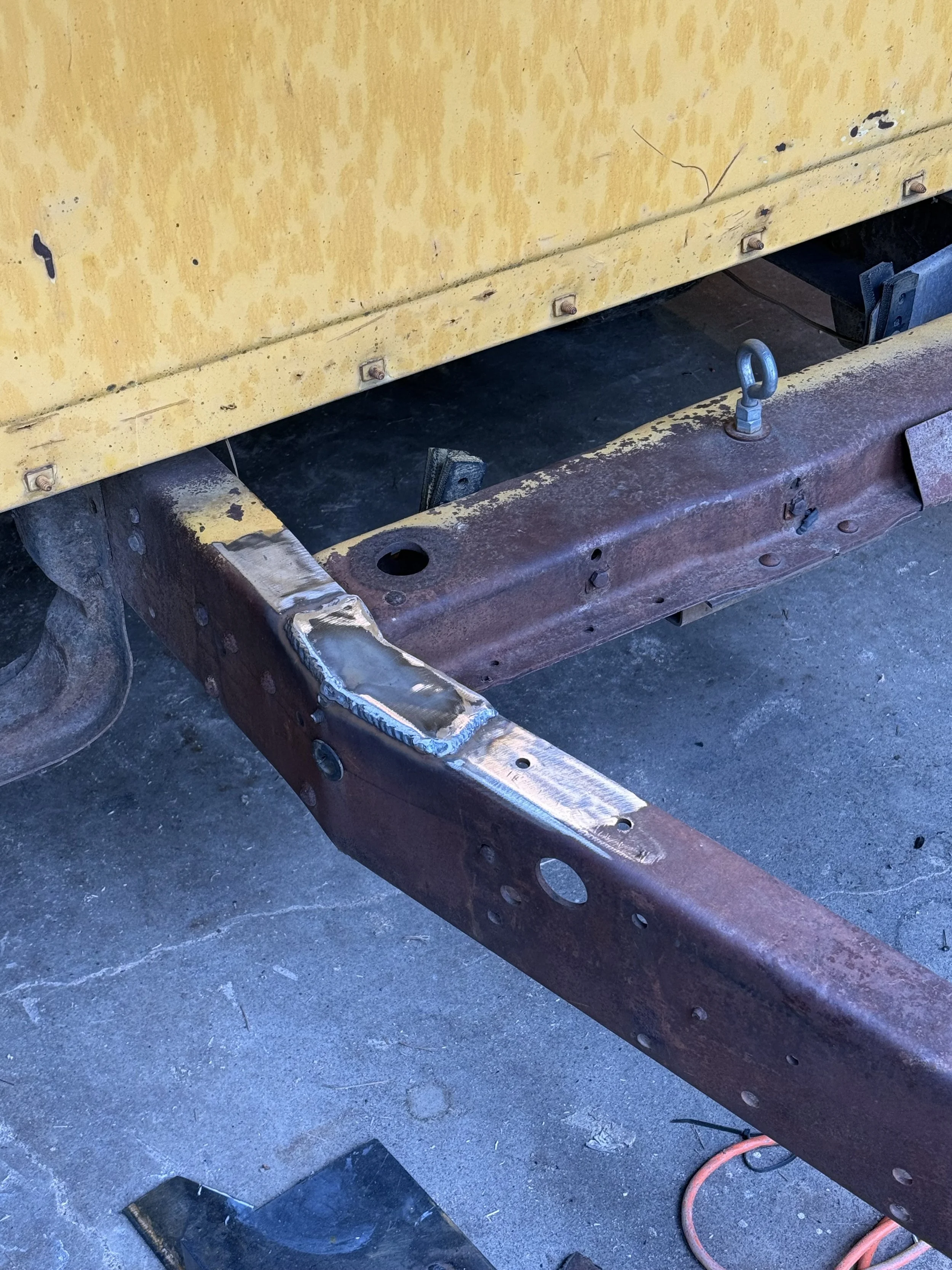 Close-up of a rusty metal frame with welding repairs and bolt holes after owner damaged old trailer.
