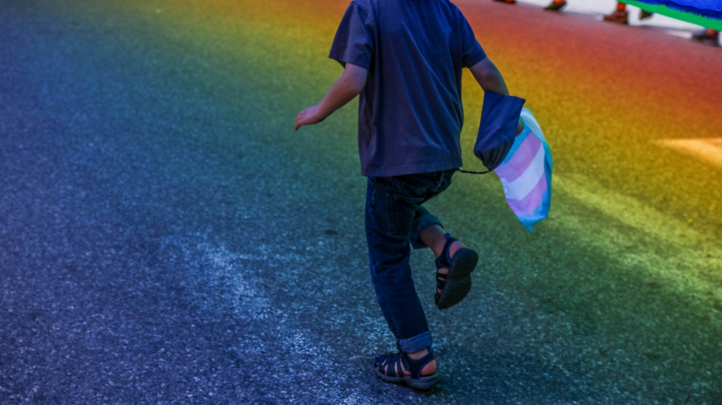 Child walking on colorful, rainbow-lit floor carrying a striped bag.