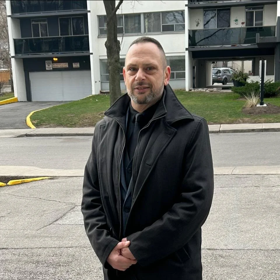 Sandor Horvath standing outdoors in front of residential buildings, wearing a dark coat, founder of LineaPrima.