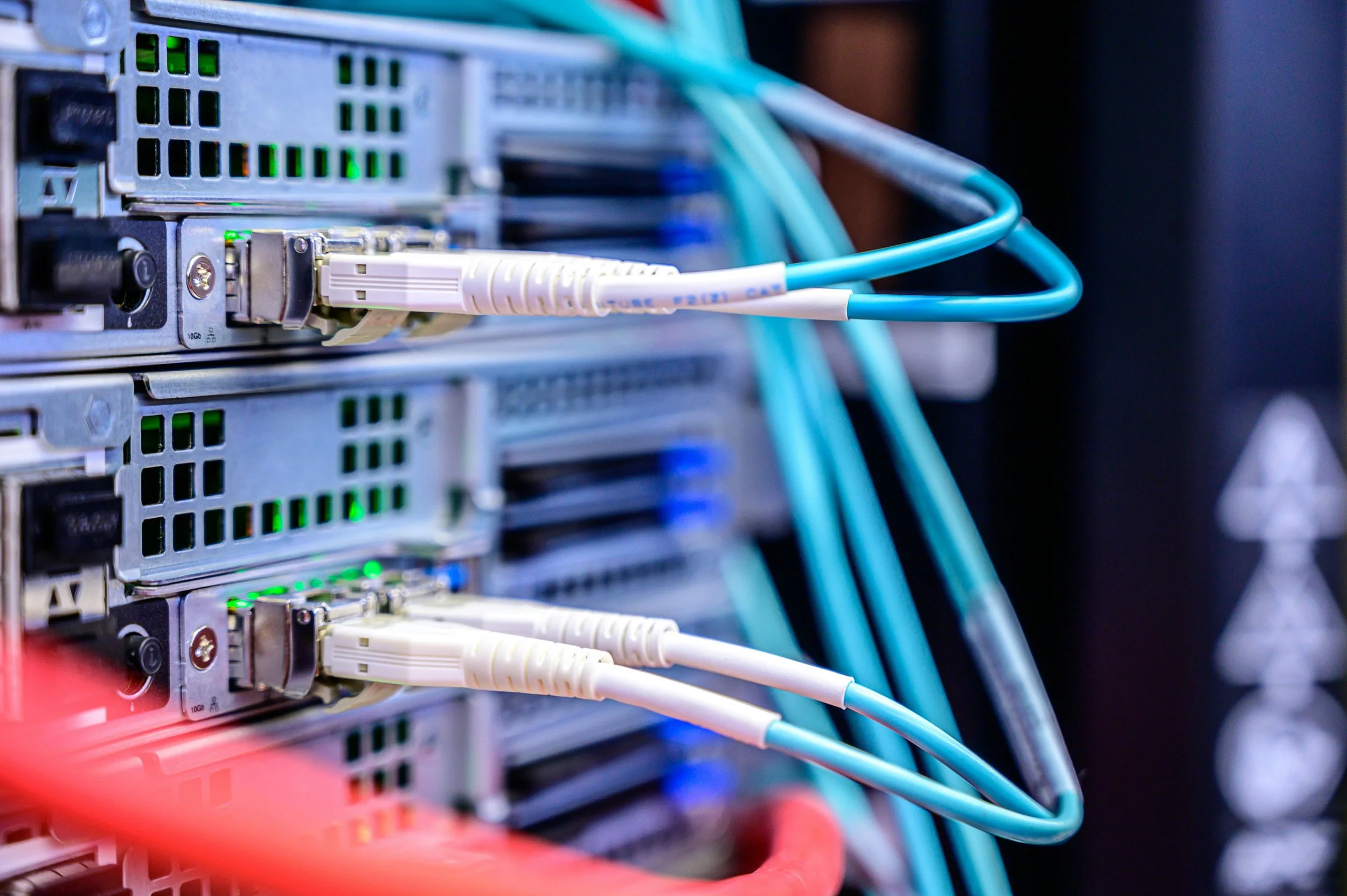 Close-up of network servers with blue Ethernet cables plugged in, illuminated green status lights, arranged in a data center or server room.