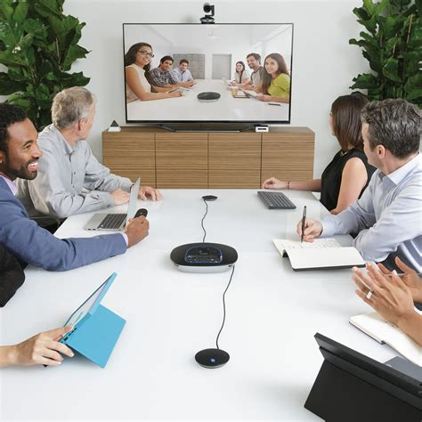 People in a conference room participating in a video call, with six people at the table and six on the screen.