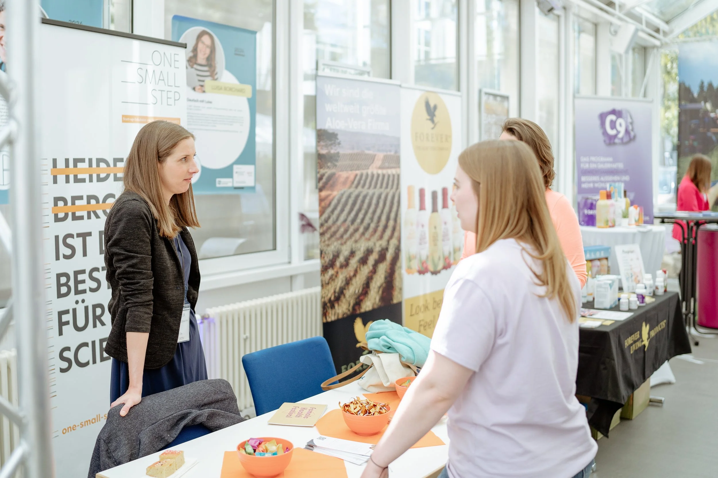 drei Frauen stehen an einem Stand auf dem Female Health Festival und unterhalten sich 