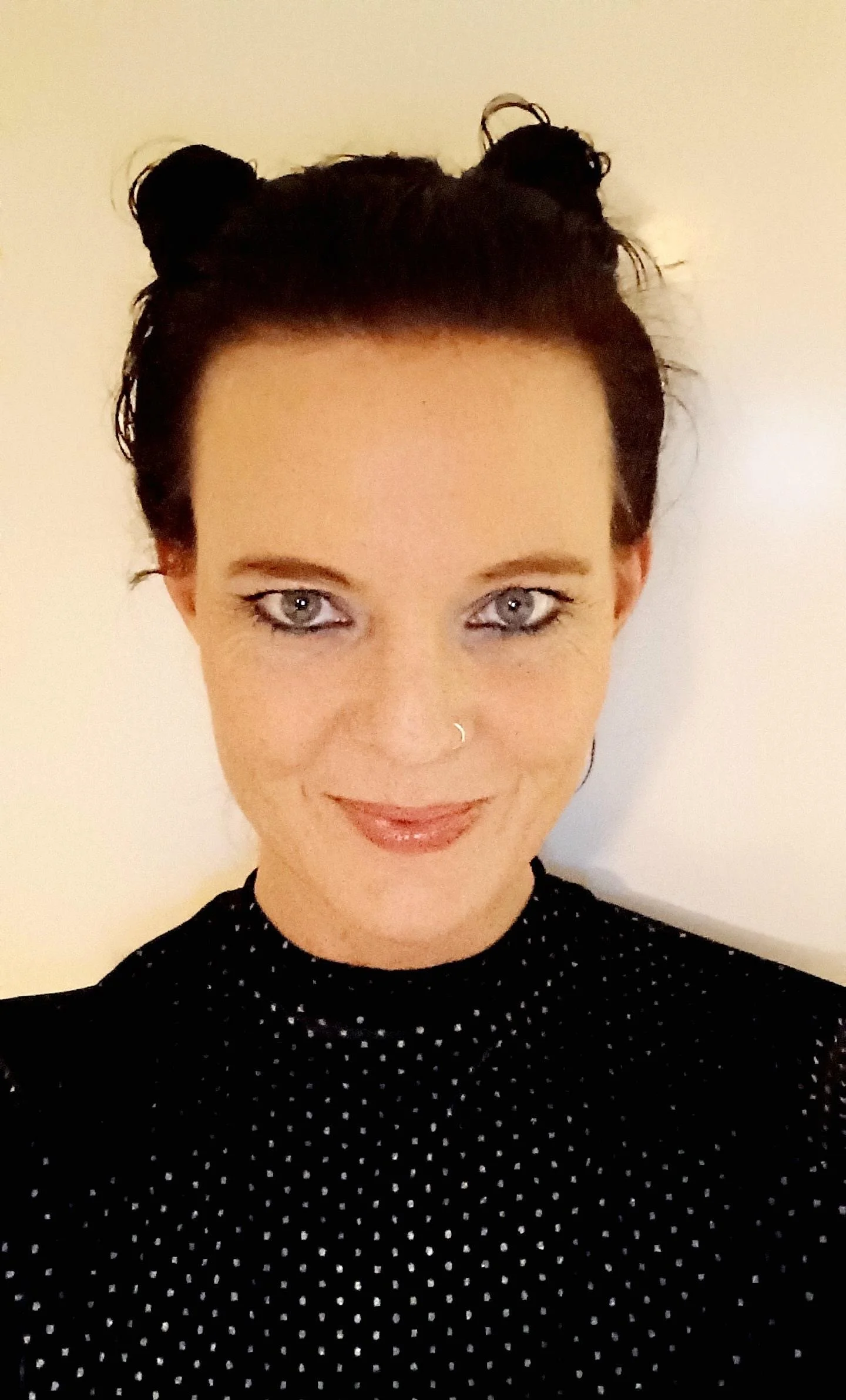 Frau mit dunklen Haaren in zwei Buns geflochten schaut verschmitzt in die Kamera