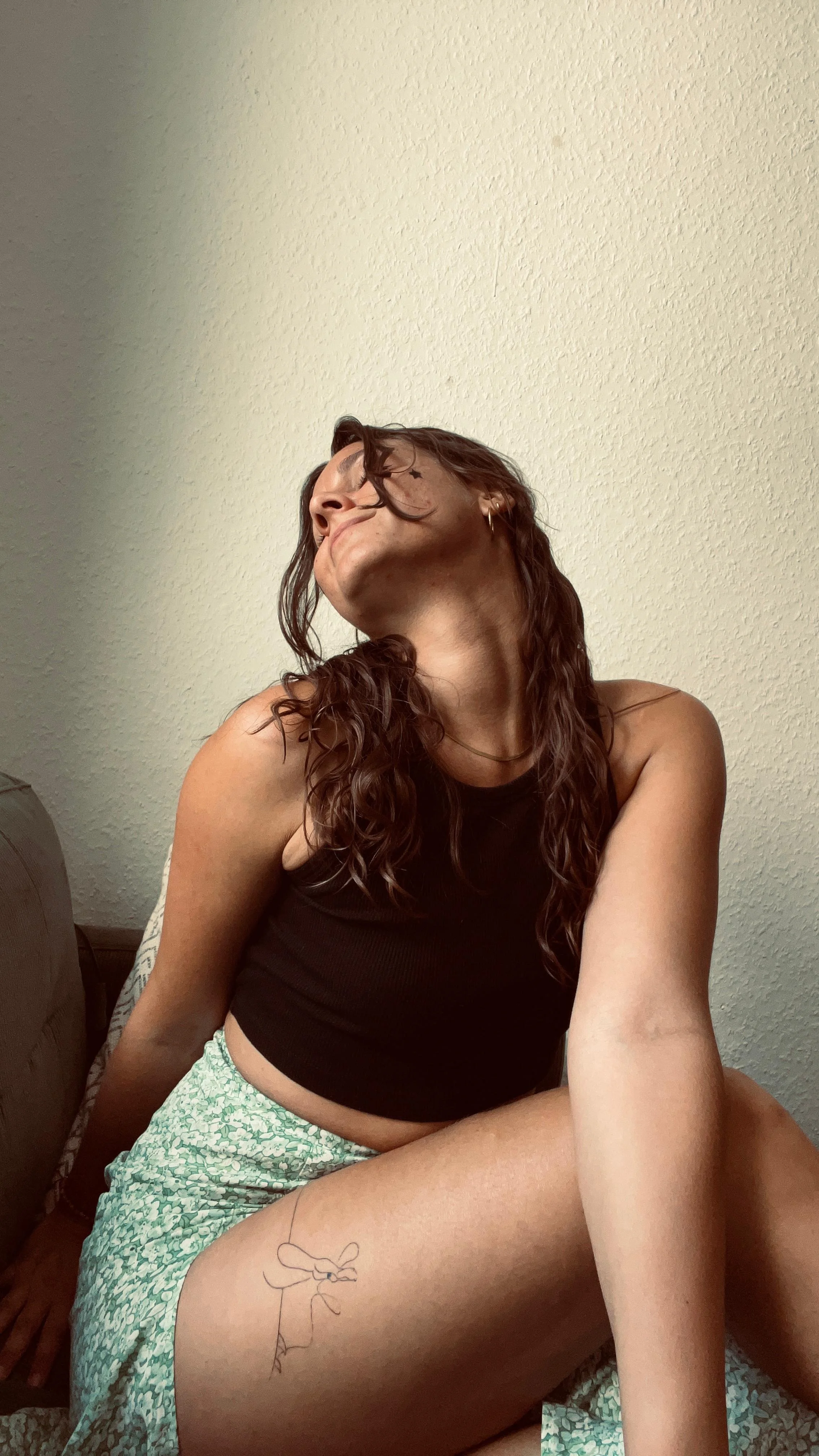 Junge Frau mit braunen Haaren und schwarzem Tank Top wirft ihre lockigen Haare nach hinten und schaut sinnlich zur Seite