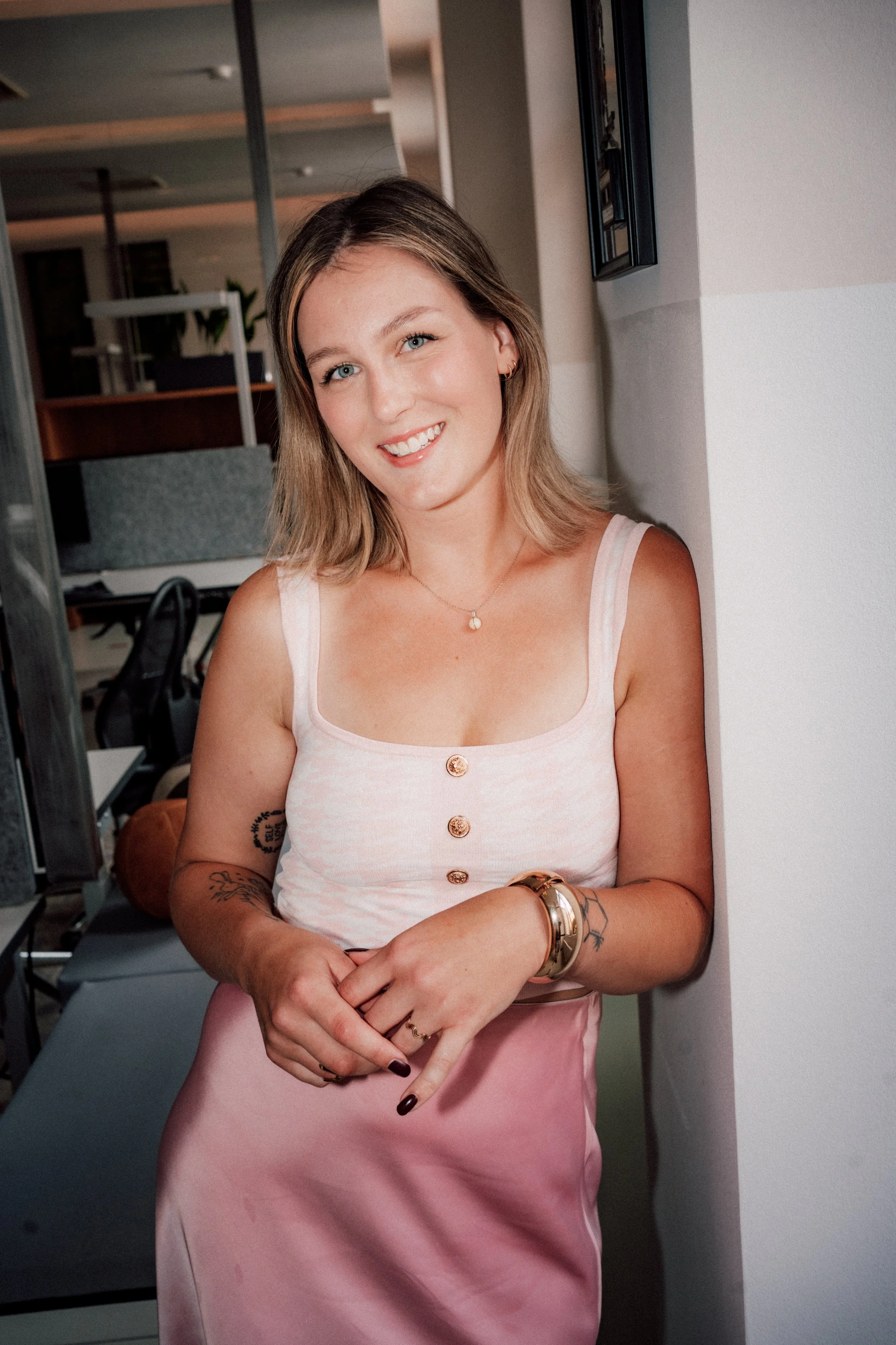 Junge Frau schaut lächelnd in die Kamera, sie trägt einen pinken Satin Rock und ein pink-weisses Oberteil mit Hahnenmuster.