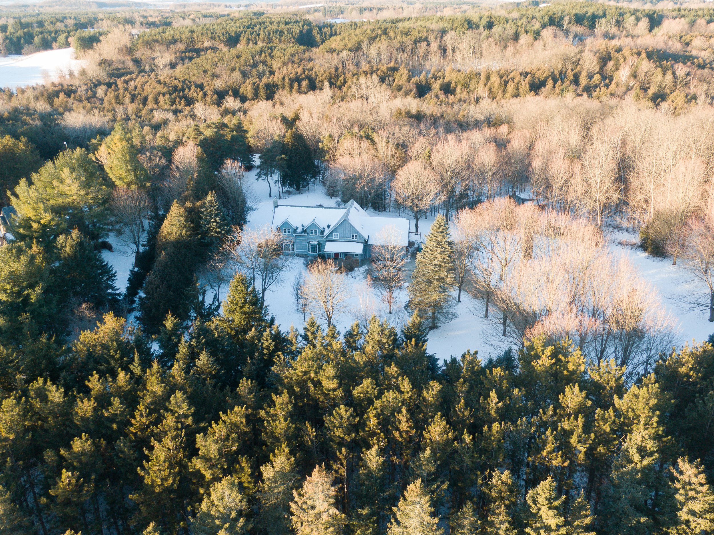 Aerial view of a large house surrounded by snow-covered trees in a forested area during winter.