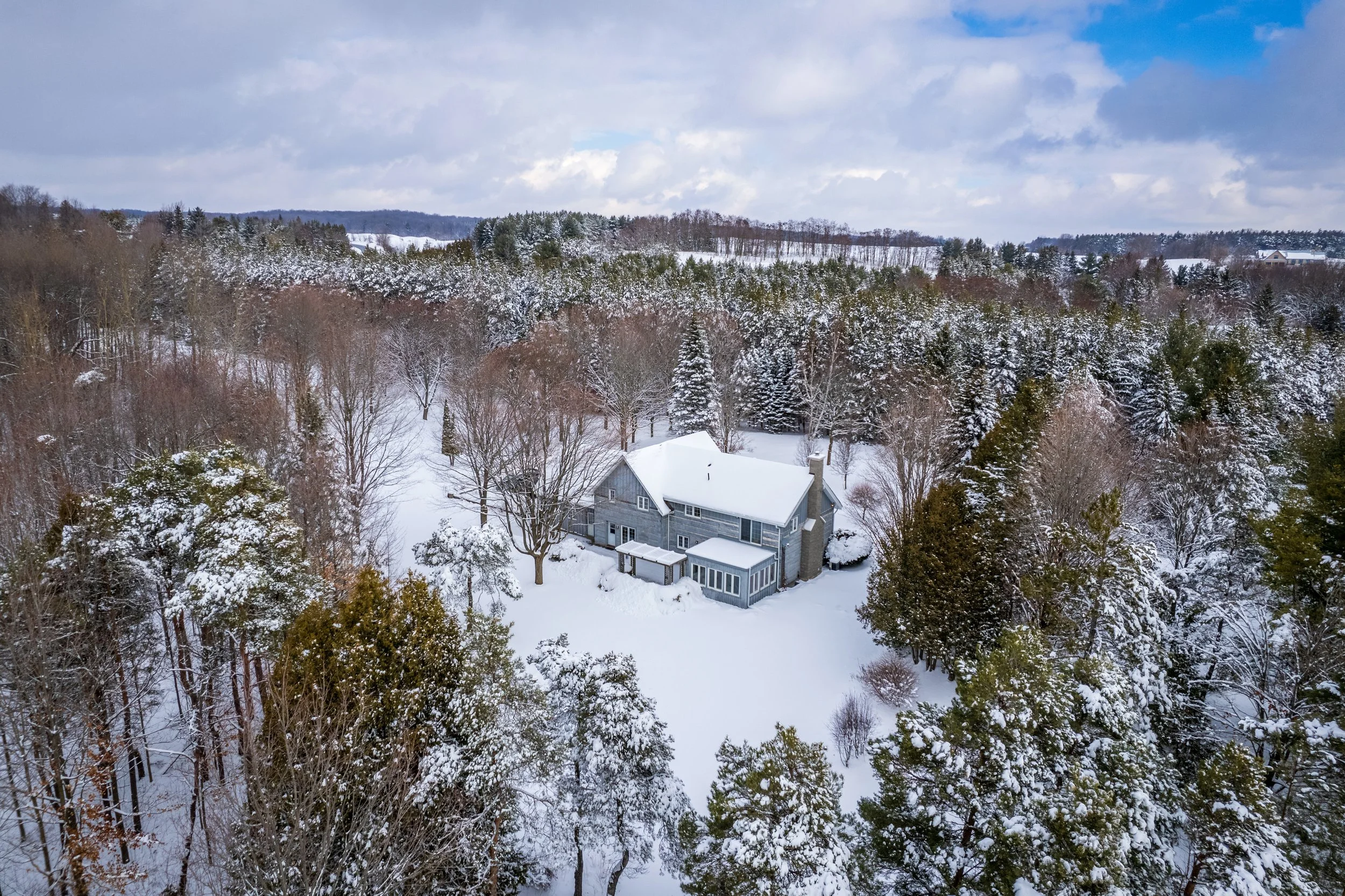 A large gray house with a snow-covered roof surrounded by snow-covered trees in a winter landscape.