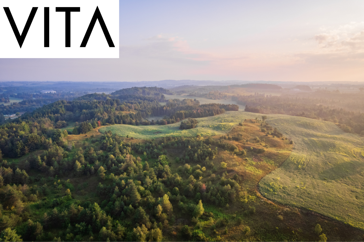 Aerial view of a landscape with rolling hills, green forests, and fields during sunset, with the VITA logo in the top left corner.
