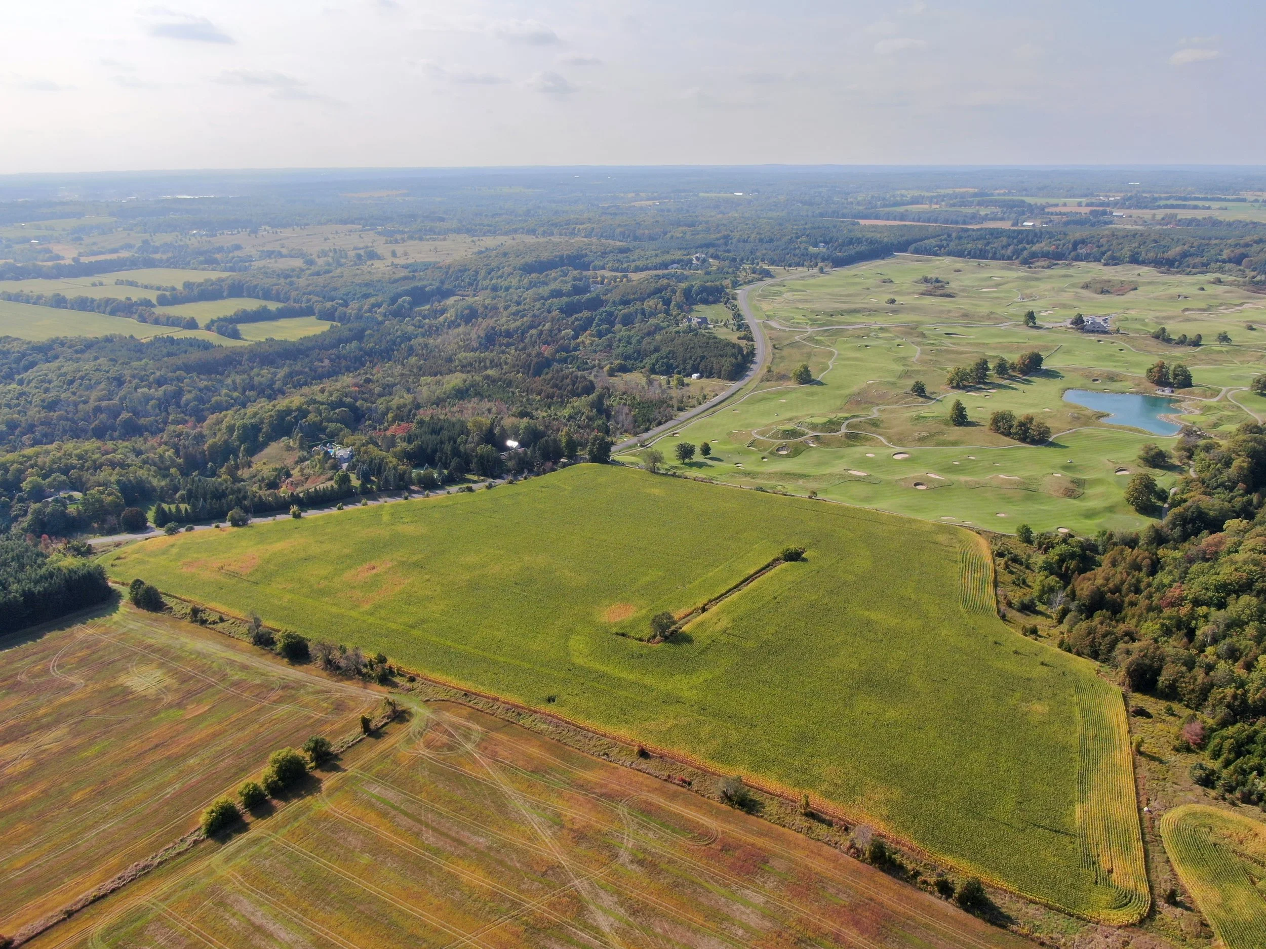 A two-story brick house with a porch, surrounded by a grassy yard with a fence, leafless trees, and a clear blue sky.