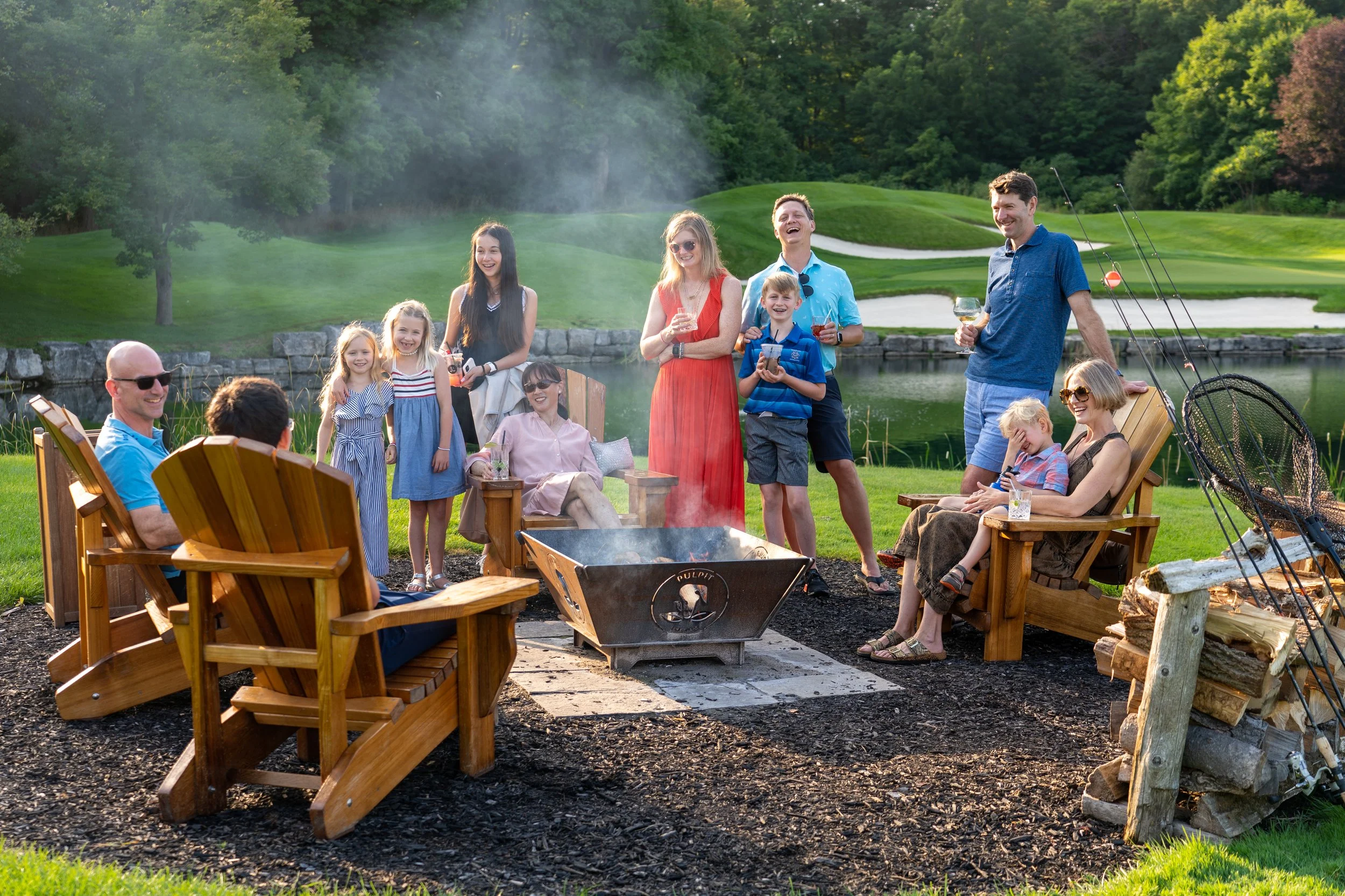 Group of people enjoying a barbecue near a pond on a green golf course with trees in the background