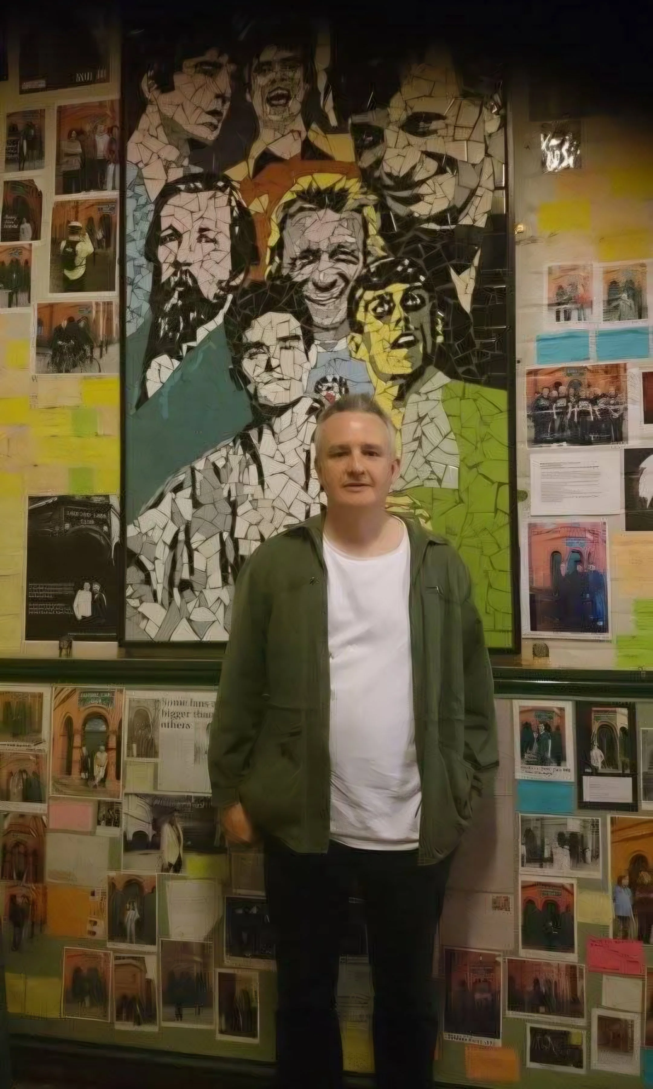 A man standing in front of a mosaic portrait wall with images of famous people, surrounded by colorful photographs and notes.