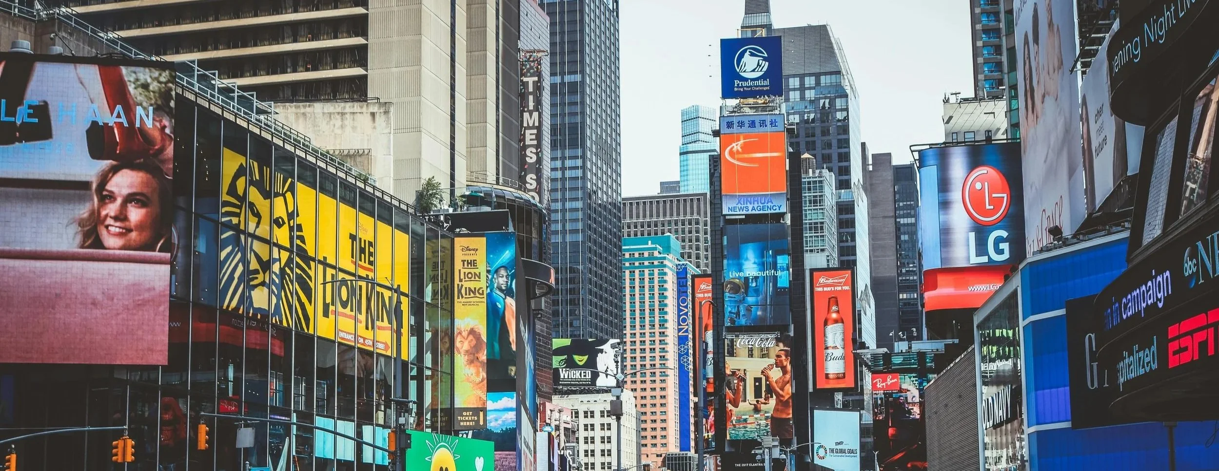 Times Square in New York City filled with colorful digital billboards and advertisements, with tall buildings and traffic lights at the intersection.