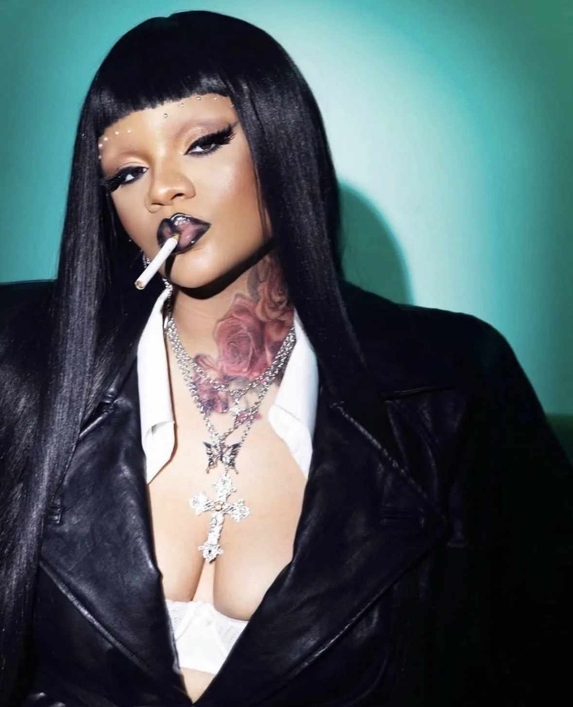 A woman with long black hair, tattoos, and layered necklaces is smoking a cigarette. She wears dark lipstick, eye makeup, a white shirt, and a black leather jacket, with a turquoise background behind her.