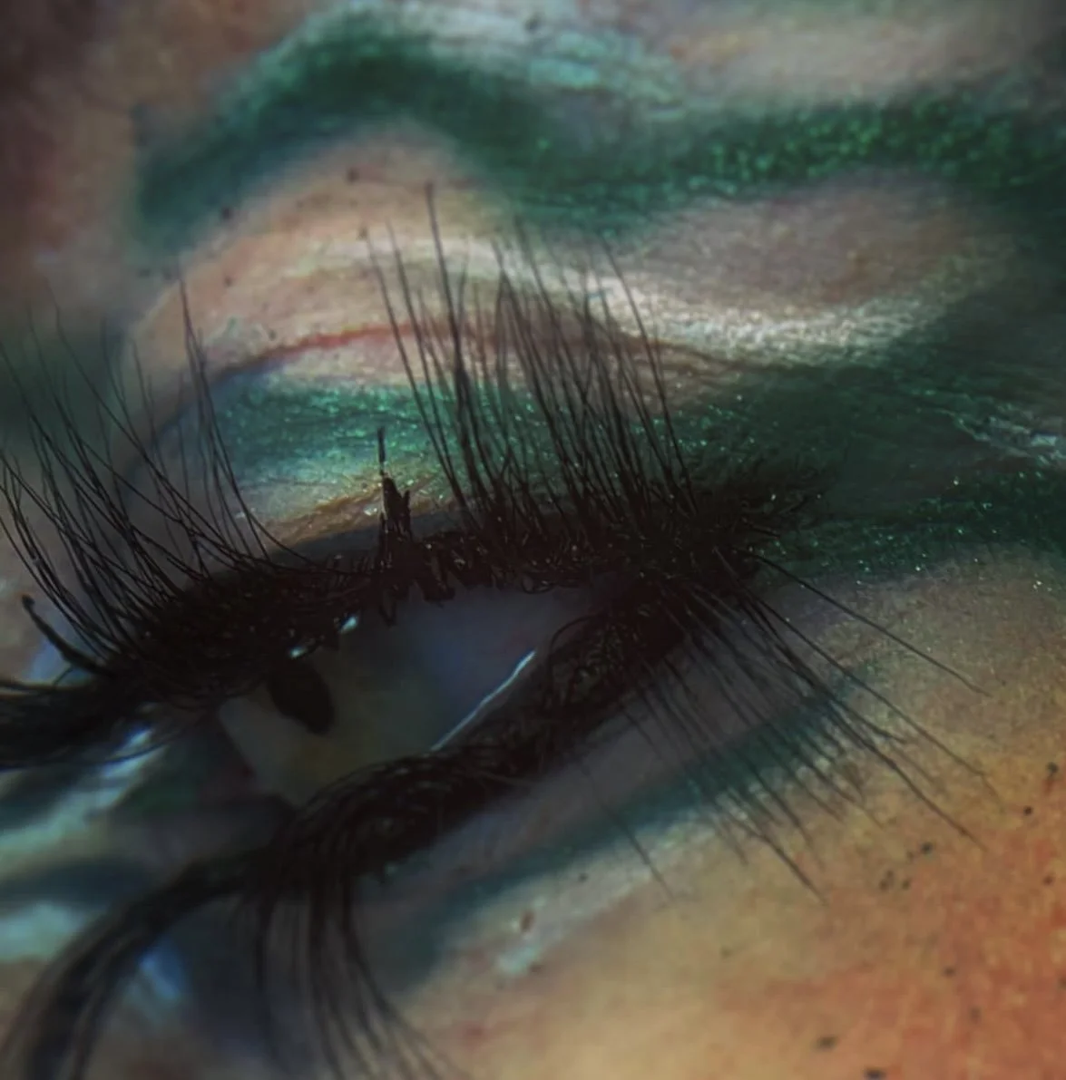 Close-up of a person's eye with vibrant, glittery green eyeshadow, long eyelashes, and a glittering eye makeup look.