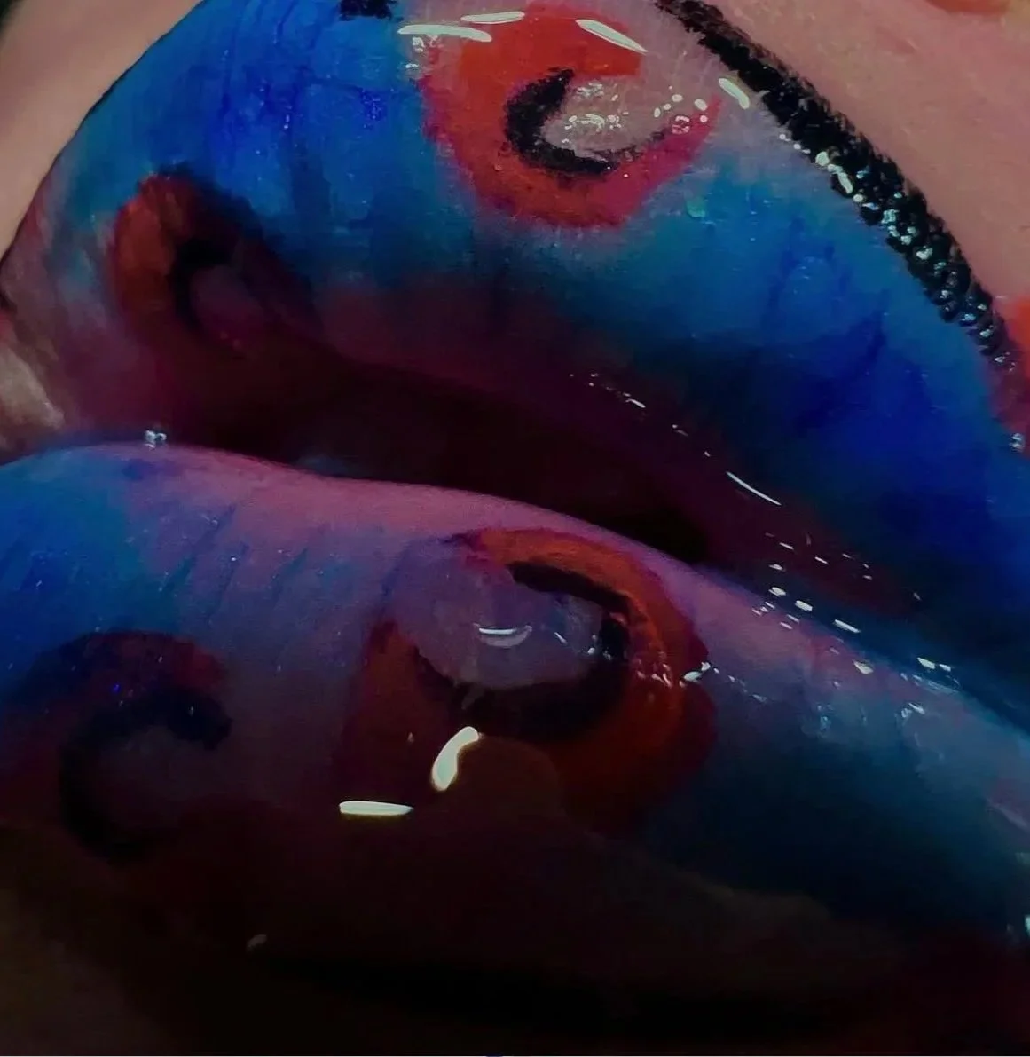 Close-up of a person's lips painted with vibrant red, blue, and black colors.