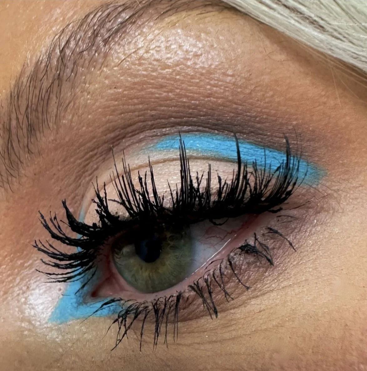 Close-up of a person's eye with makeup, including black mascara on the eyelashes and bright blue eyeshadow applied along the upper eyelid and lower lash line.