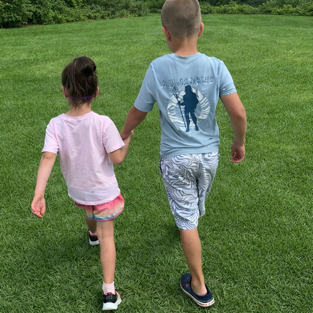 Two children, a girl and a boy, walking hand in hand across a grassy field with trees in the background.