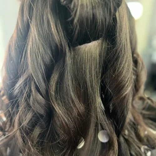 Close-up of styled, wavy brown hair with highlights in a salon setting.