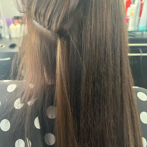 Side view of a woman with medium brown hair, some sections highlighted in light brown, in a salon setting.