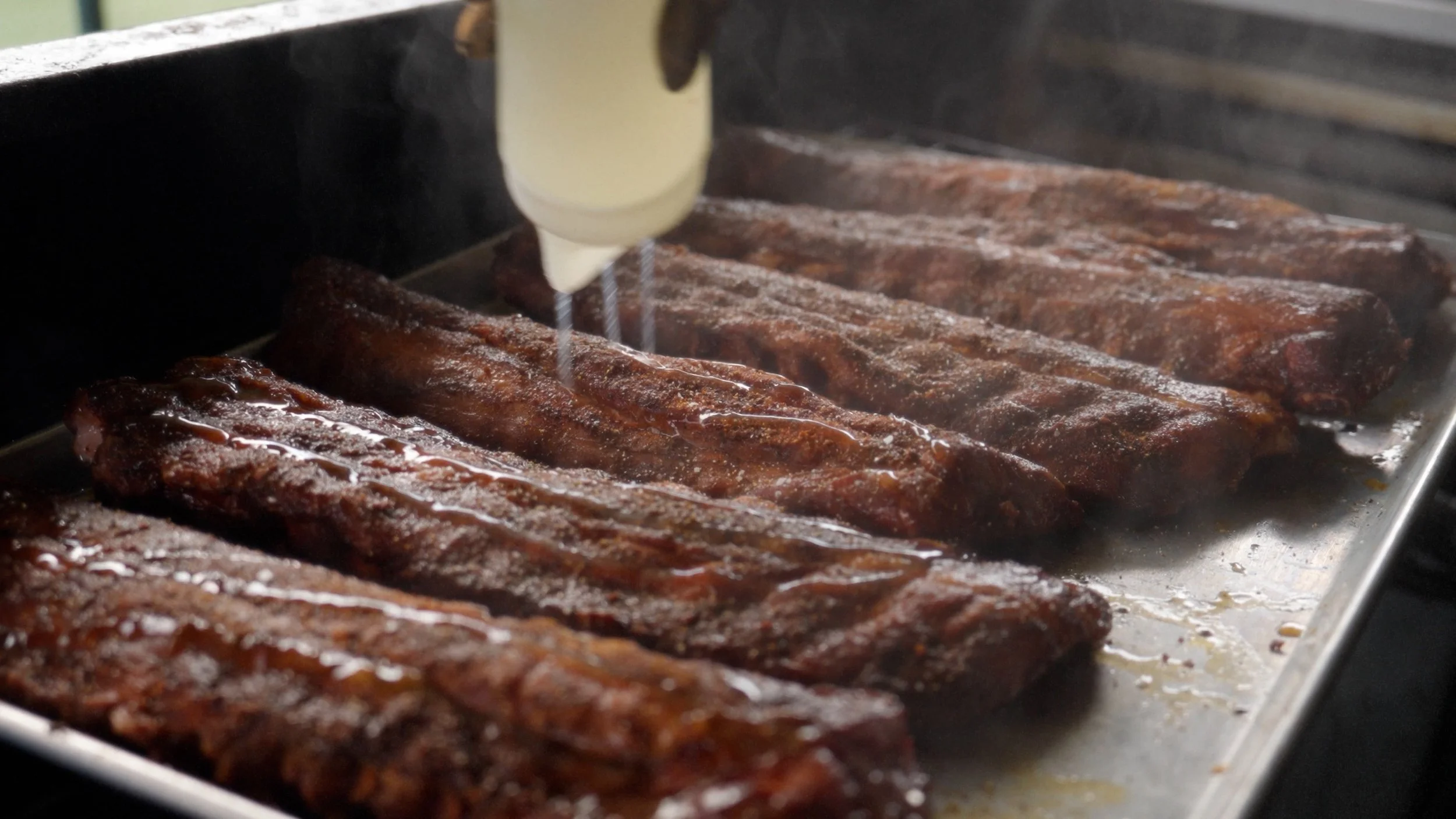 Meat ribs being basted with sauce on a grill.