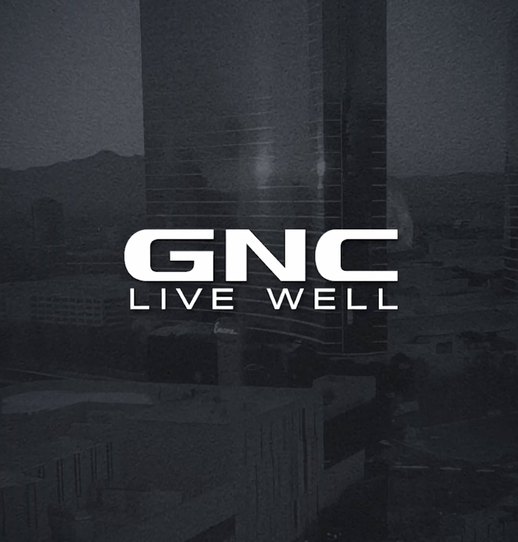 GNC logo with the slogan "Live Well" against a dark cityscape background.