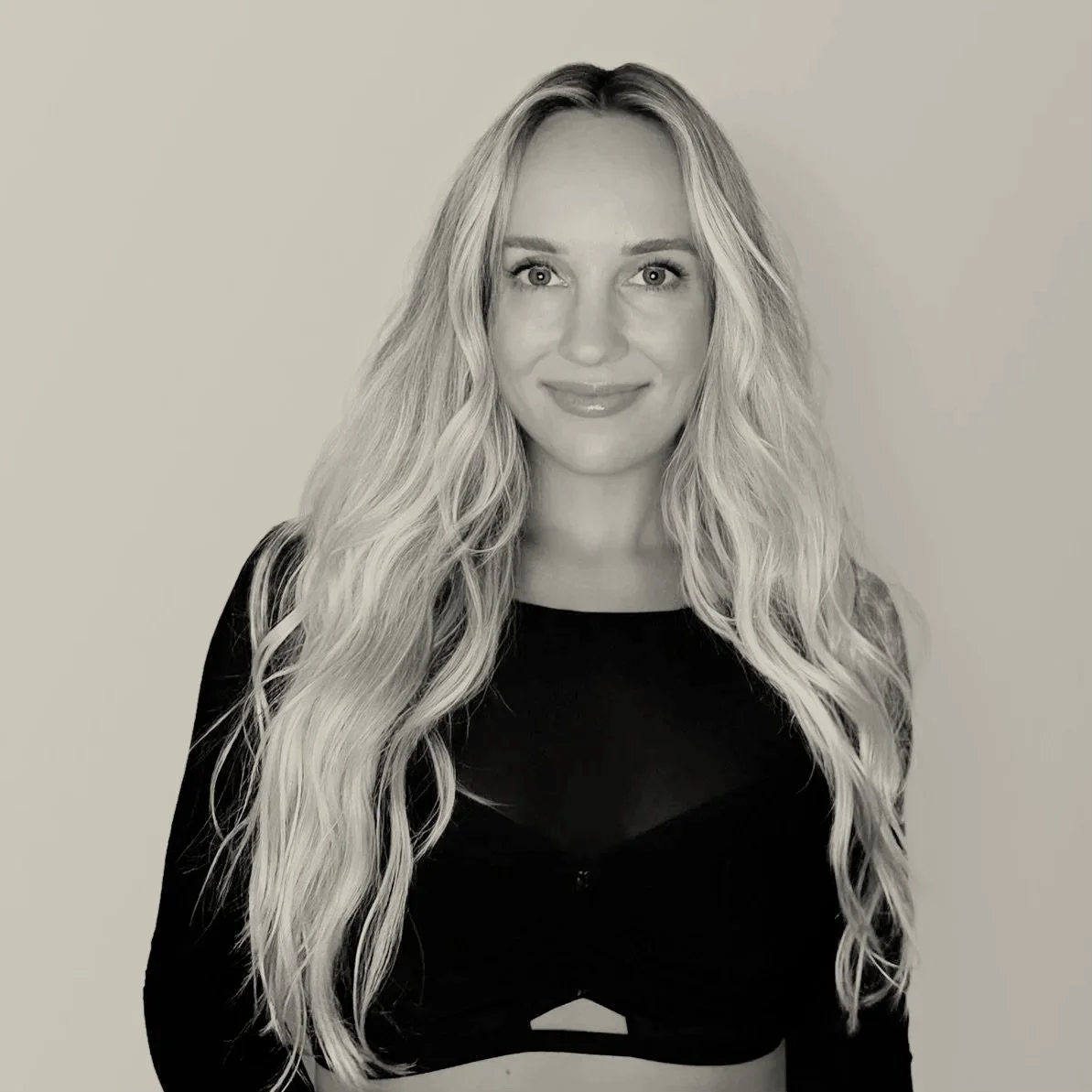 Black and white photo of a woman with long, wavy hair, wearing a black top, smiling at the camera.