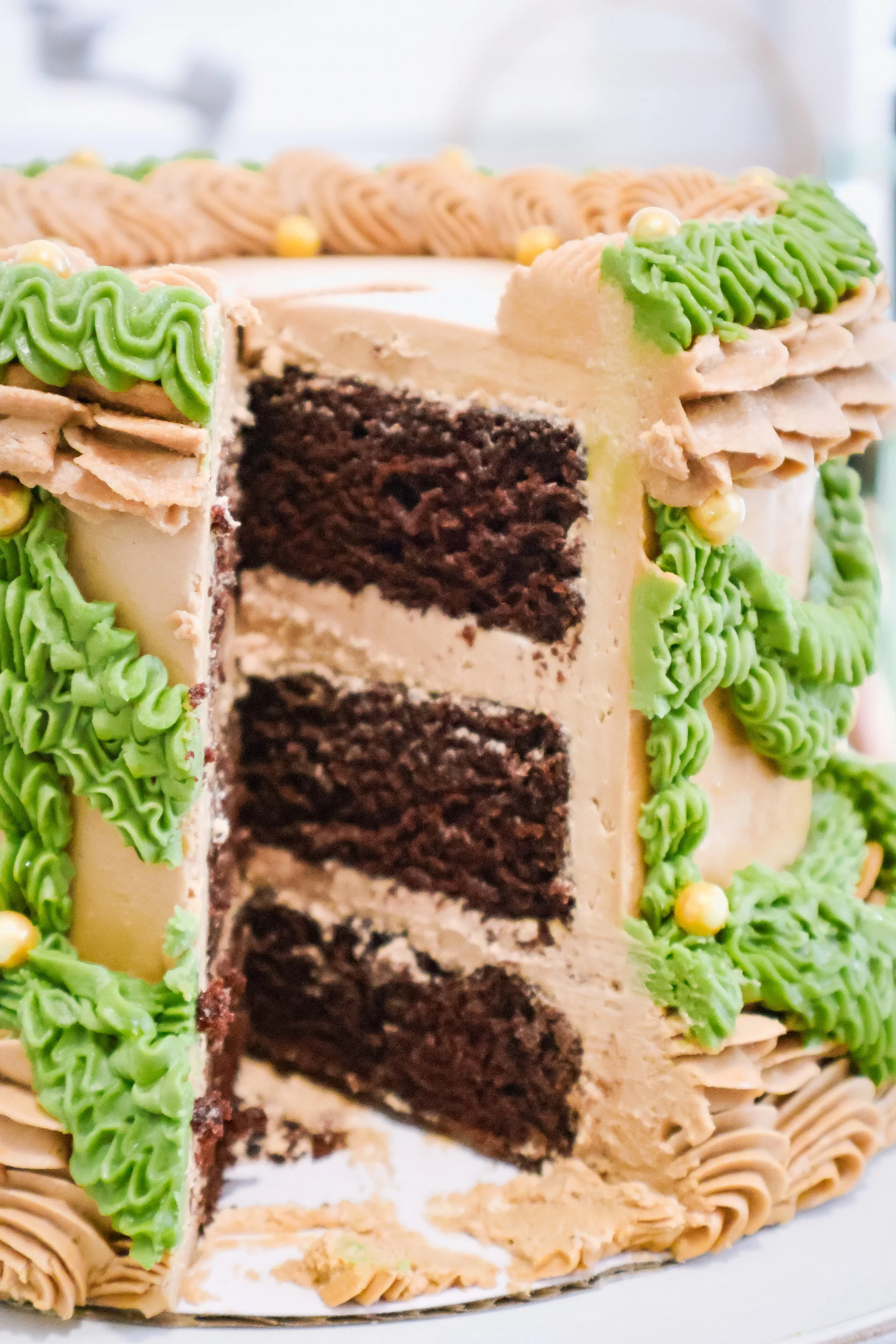 Decorative cake with brown and green buttercream swirls. Slice taken out og chocolate cake